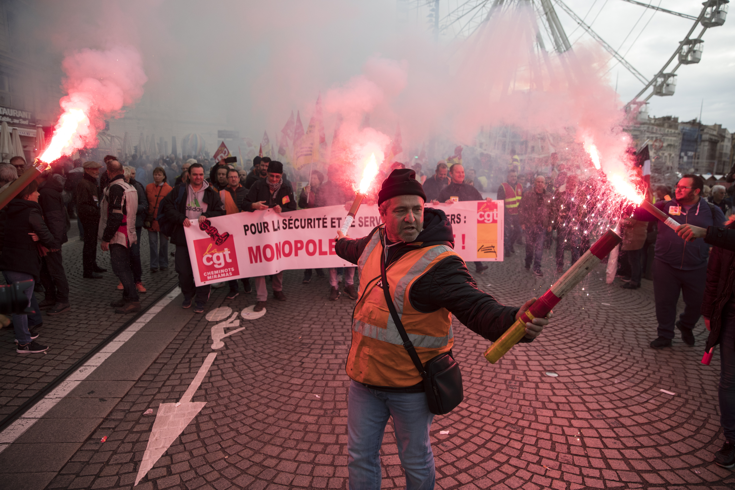 A railworker holds a flare during a mass stirke in the Old Port of Marseille, southern France, Wednesday, Dec. 5, 2019. Workers across the public sector fear President Emmanuel Macron's reform will force them to work longer and shrink their pensions. AP Photo/Daniel Cole)