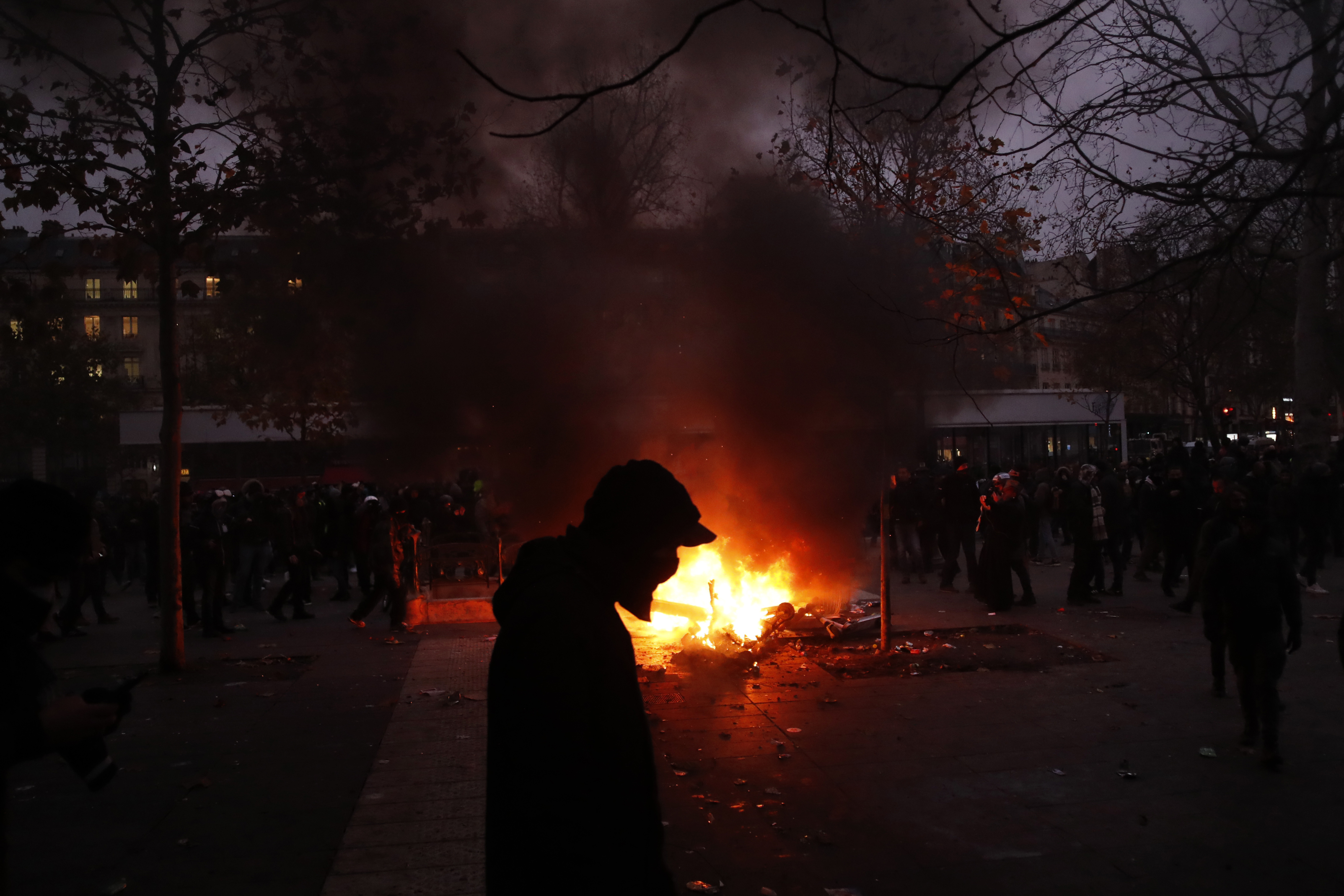 A demonstrator walks past a fire during a demonstration in Paris, Thursday, Dec. 5, 2019. The Eiffel Tower shut down, France's high-speed trains stood still and tens of thousands of people marched through Paris and other cities Thursday, in a massive and sometimes chaotic outpouring of anger at the government's plan to overhaul the retirement system. (AP Photo/Thibault Camus)