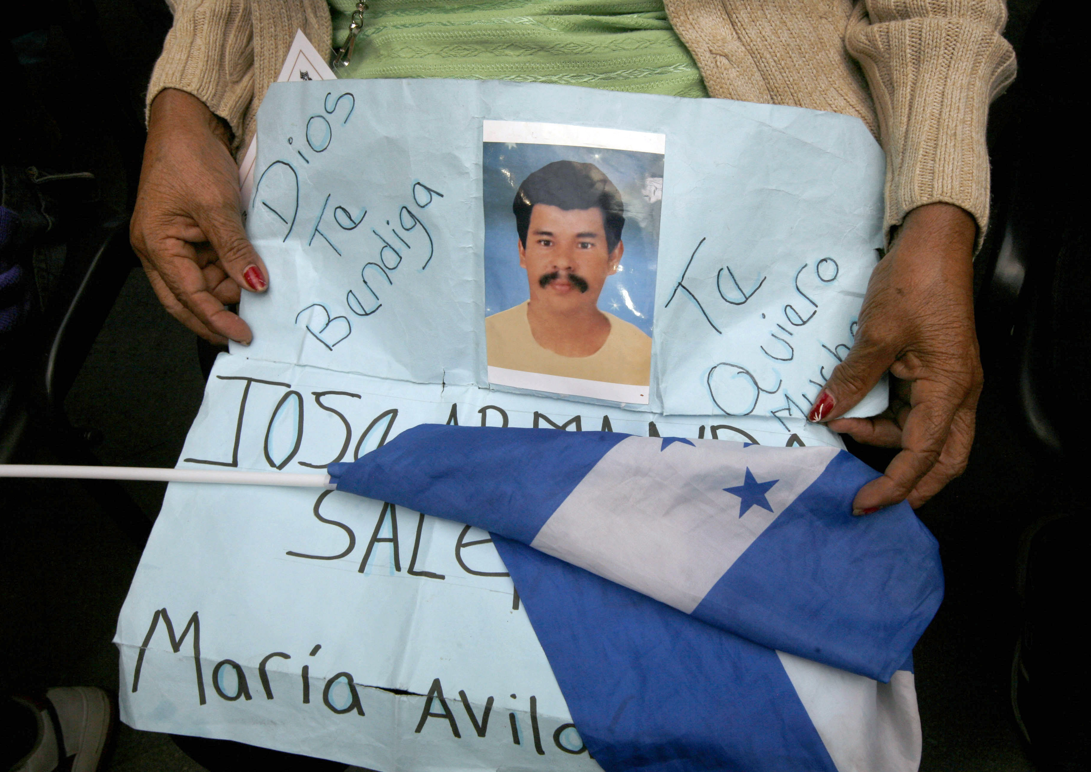 Migrant Maria Avila holds a sign with an image of his missing son, Jose Salgado Avila and a Honduran flag in Mexico City, Monday, Aug. 1, 2011. Hundreds of Central American relatives of dead or missing migrants traveled to Mexico CIty in an effort to pressure Mexican authorities to do more to guarantee the human rights of migrants traveling north towards the United States. (AP Photo/ Marco Ugarte)