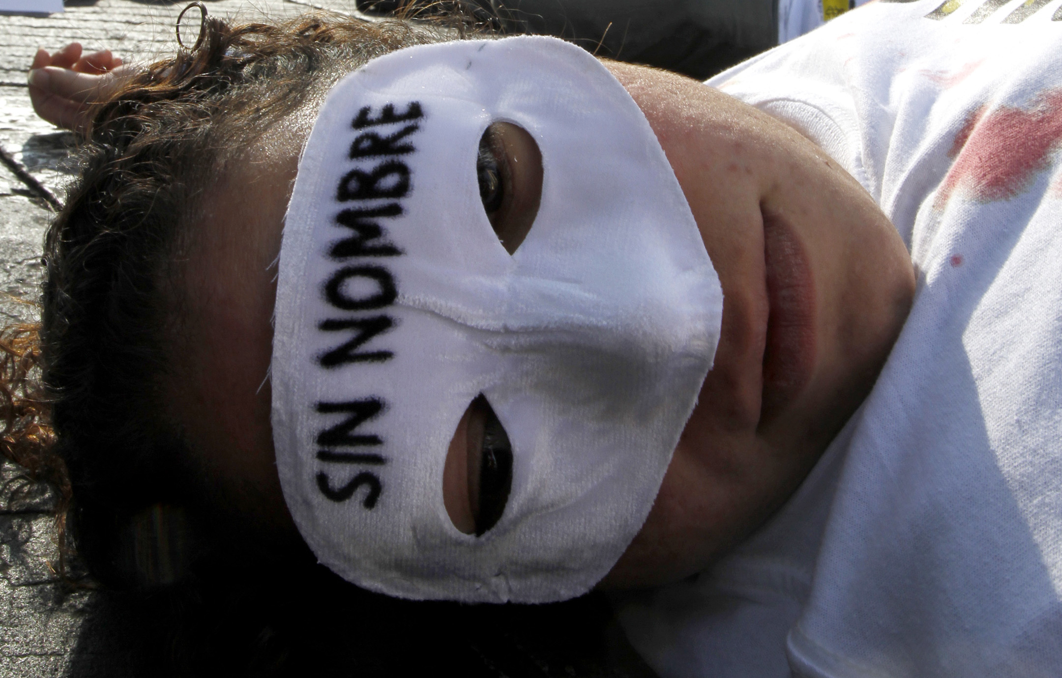 A demonstrator, lying on the floor, wears a mask that reads in Spanish 