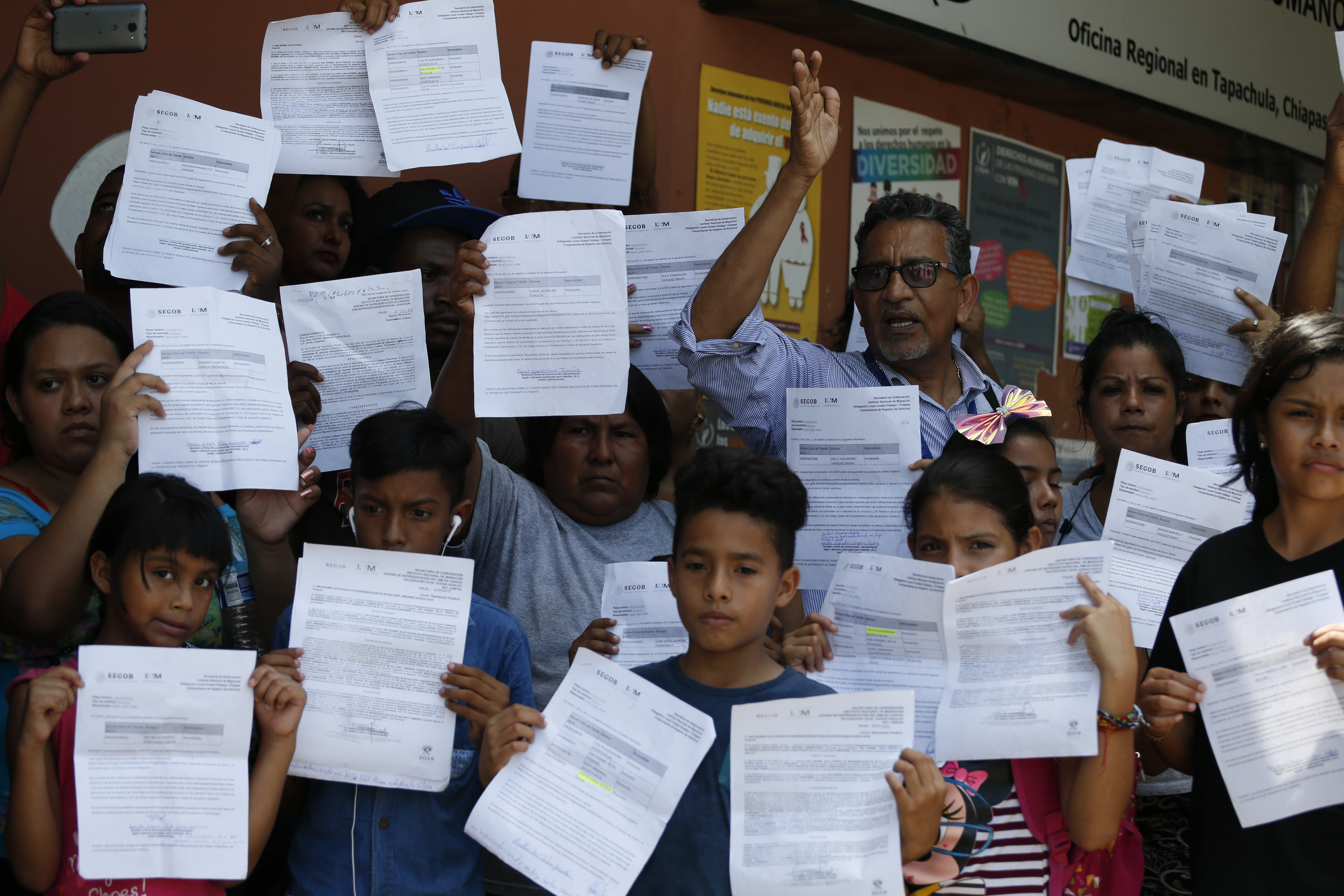 Human rights activist Luis Villagran speaks as migrants hold up their Mexican migration paperwork during a small protest against long wait times for receiving documents to legally stay in Mexico, outside the office of the national Human Rights Commission in Tapachula, Mexico, Wednesday, June 19, 2019. Villagran led a group of several dozens migrants to the offices to protest in front of the press, before entering with a representative group of migrants from several countries to present the group's complaints.(AP Photo/Rebecca Blackwell)
