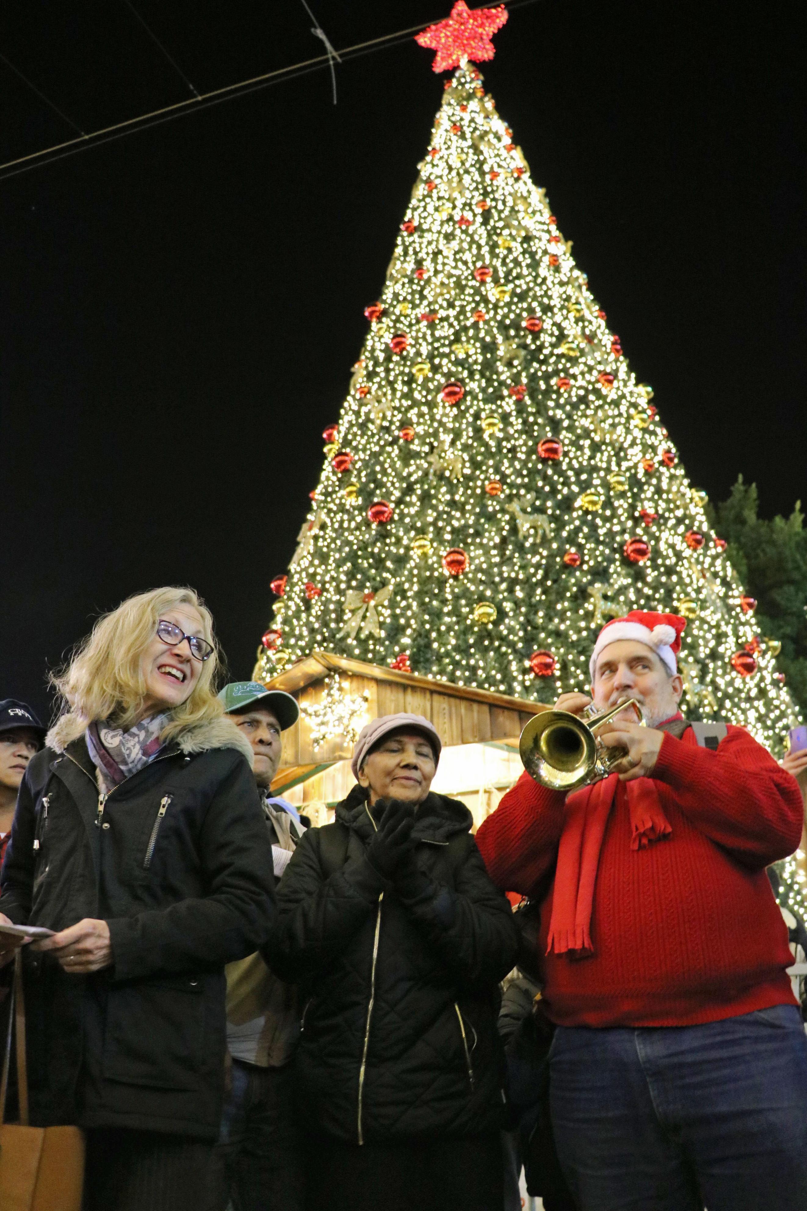 People sing in front of a Christmas tree near the Church of the Nativity in Bethlehem on Dec. 24, 2019. (Kyodo via AP Images) ==Kyodo