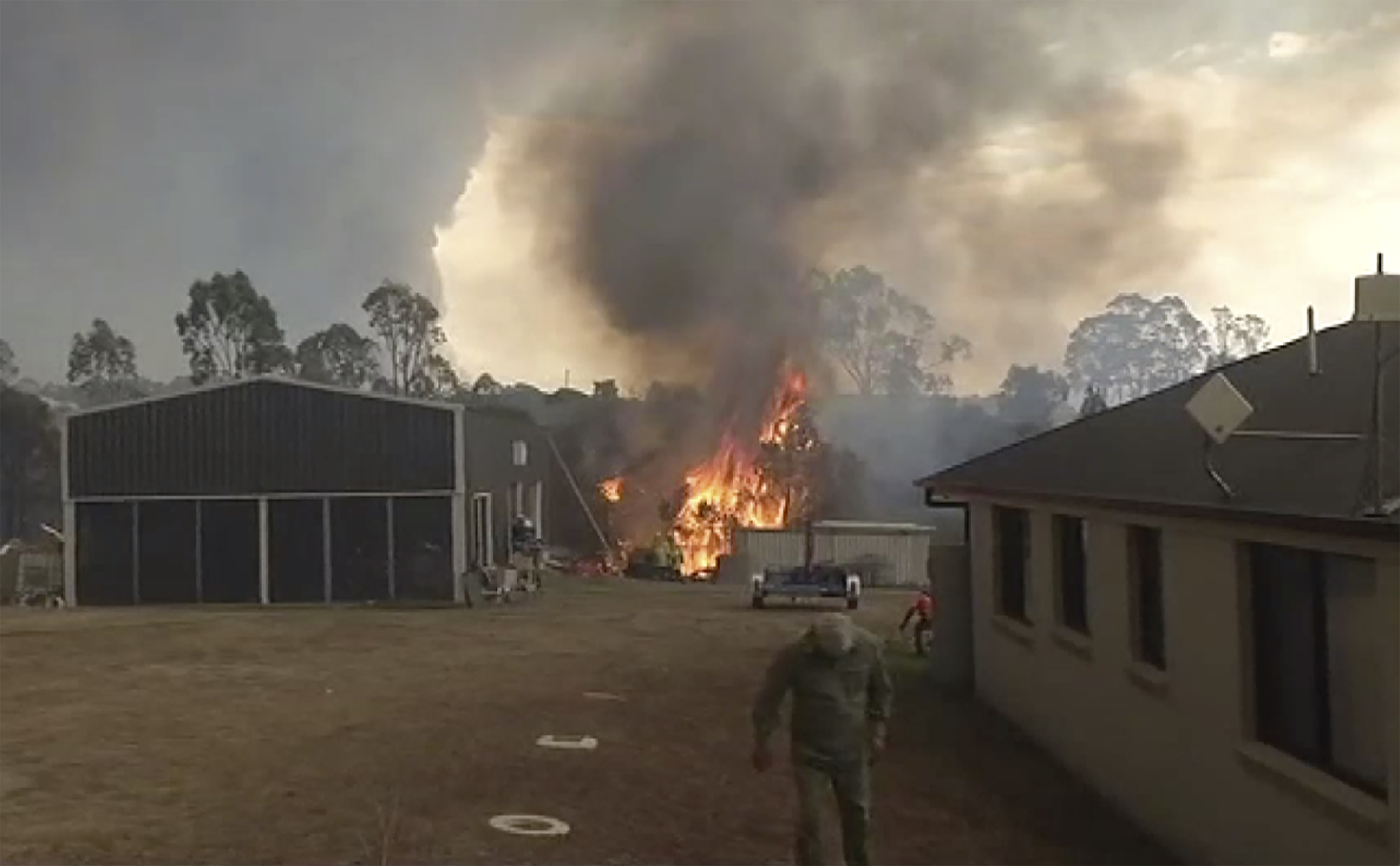 In this image made from video, a fire is extinguished behind a house in Mollymook, New south Wales, Australia, Tuesday, Derc. 31, 2019. Wildfires burning across Australia's two most-populous states have trapped residents of a seaside town in apocalyptic conditions, destroyed many properties and caused at least two fatalities. (Australian Broadcasting Corporation, Channel 9, Channel 7 via AP)