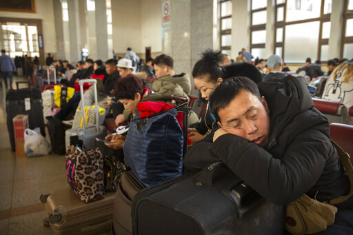 A traveler rests on his suitcase in a waiting room at the Beijing Railway Station in Beijing, Friday, Jan. 17, 2020. As the Lunar New Year approached, Chinese travelers flocked to train stations and airports Friday to take part in a nationwide ritual: the world's biggest annual human migration. (AP Photo/Mark Schiefelbein)
