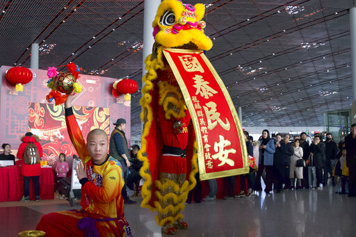 Travelers watch a lion dance performance at Beijing Capital International Airport in Beijing, Friday, Jan. 17, 2020. As the Lunar New Year approached, Chinese travelers flocked to train stations and airports Friday to take part in a nationwide ritual: the world's biggest annual human migration. (AP Photo/Ng Han Guan)