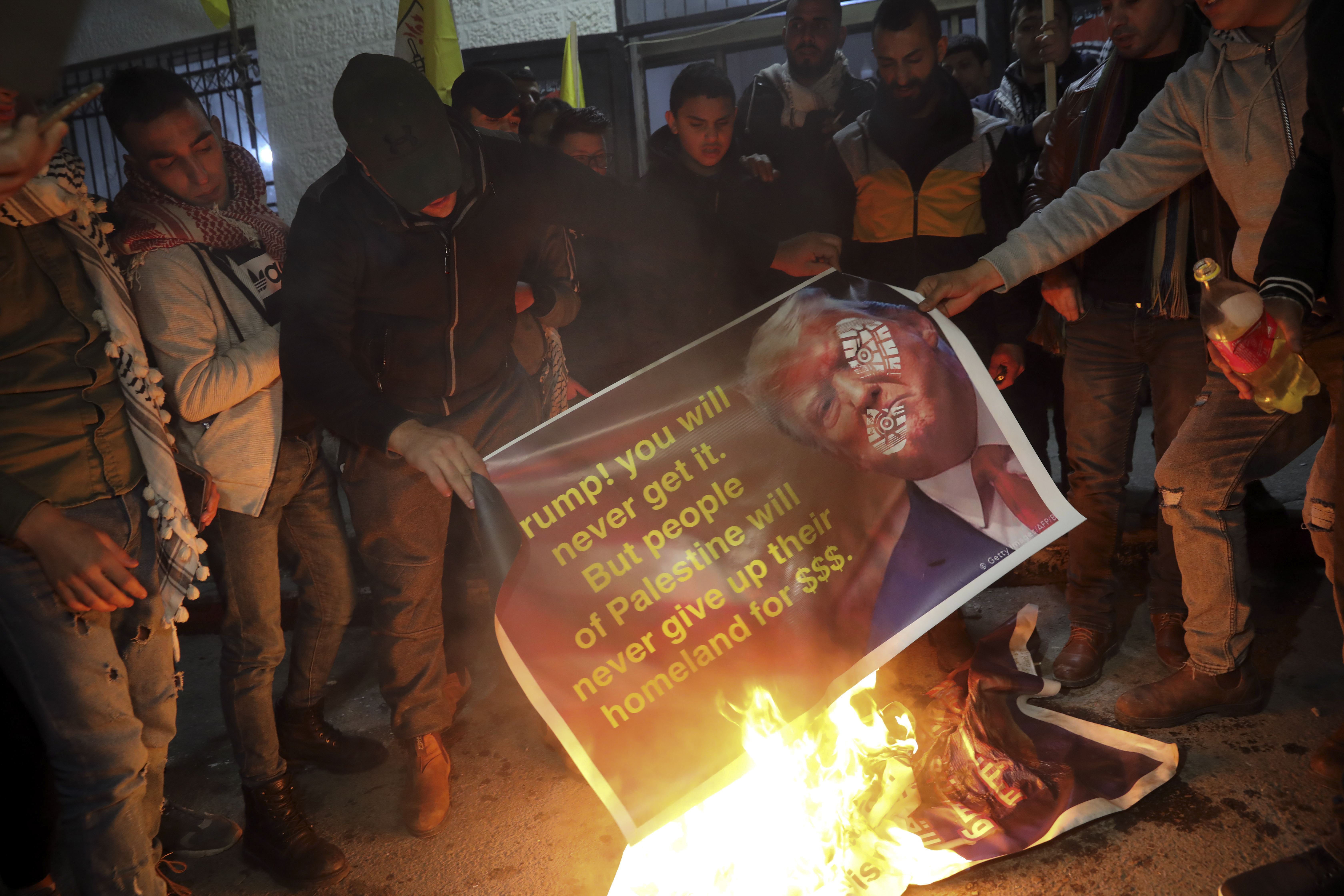 Palestinian burn a poster showing U.S. President Donald Trump as they protest the American peace plan in Bethlehem, Monday, Jan. 27, 2020. Israeli Prime Minister Benjamin Netanyahu arrived in Washington Sunday night vowing to 