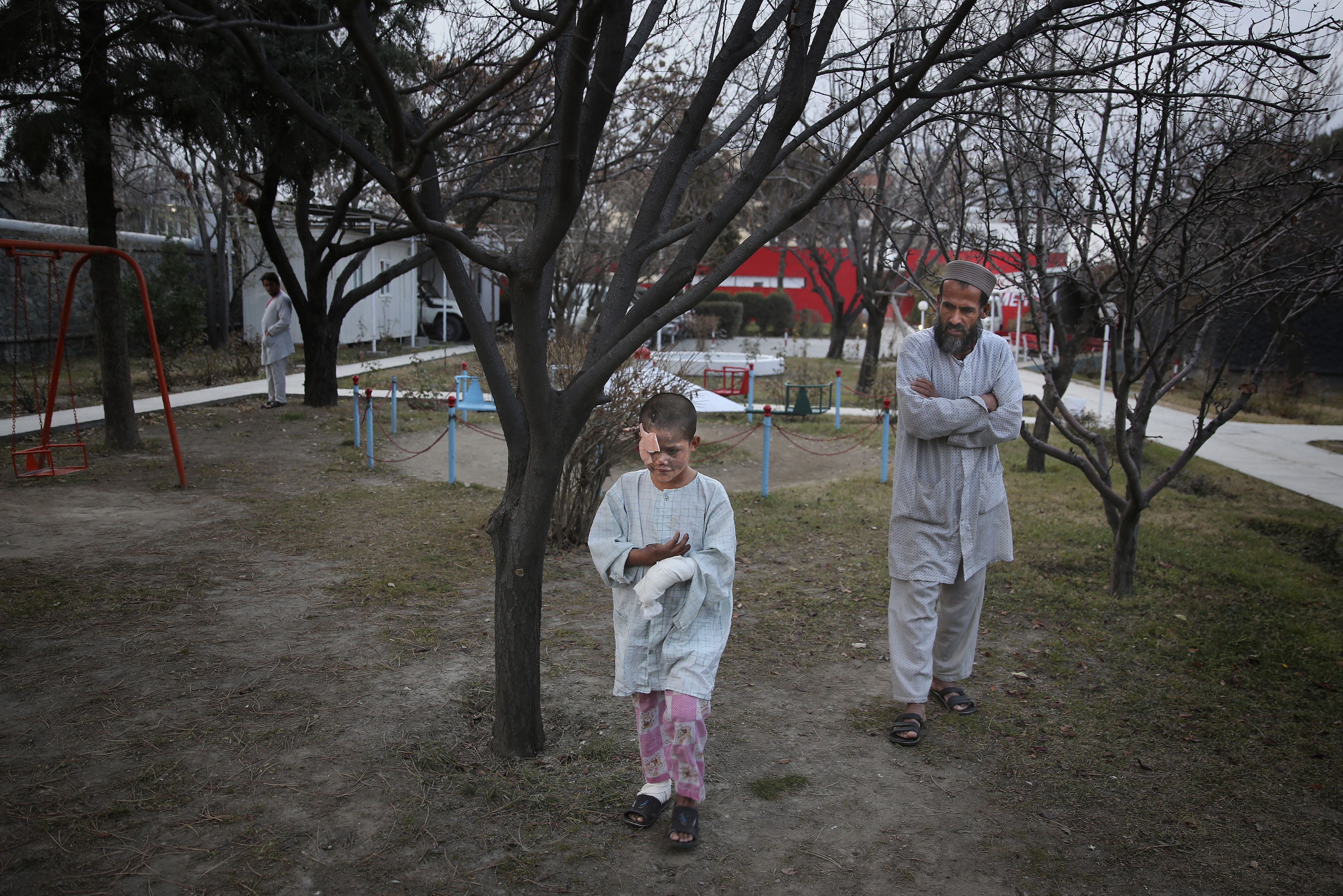 In this Thursday, Dec. 12, 2019, photo, Ismatullah follows his nine-year-old son Eimal, who has lost his right eye and several fingers on his hands in a landmine blast, as he tries to walk in the compound of Emergency Surgical Center for Civilian War Victims in Kabul, Afghanistan. The total number of children killed or maimed in more than four decades long Afghan war is not known. But, with a population where close to 50% are under the age of 20, the losses among the young is tremendous. (AP Photo/Altaf Qadri)
