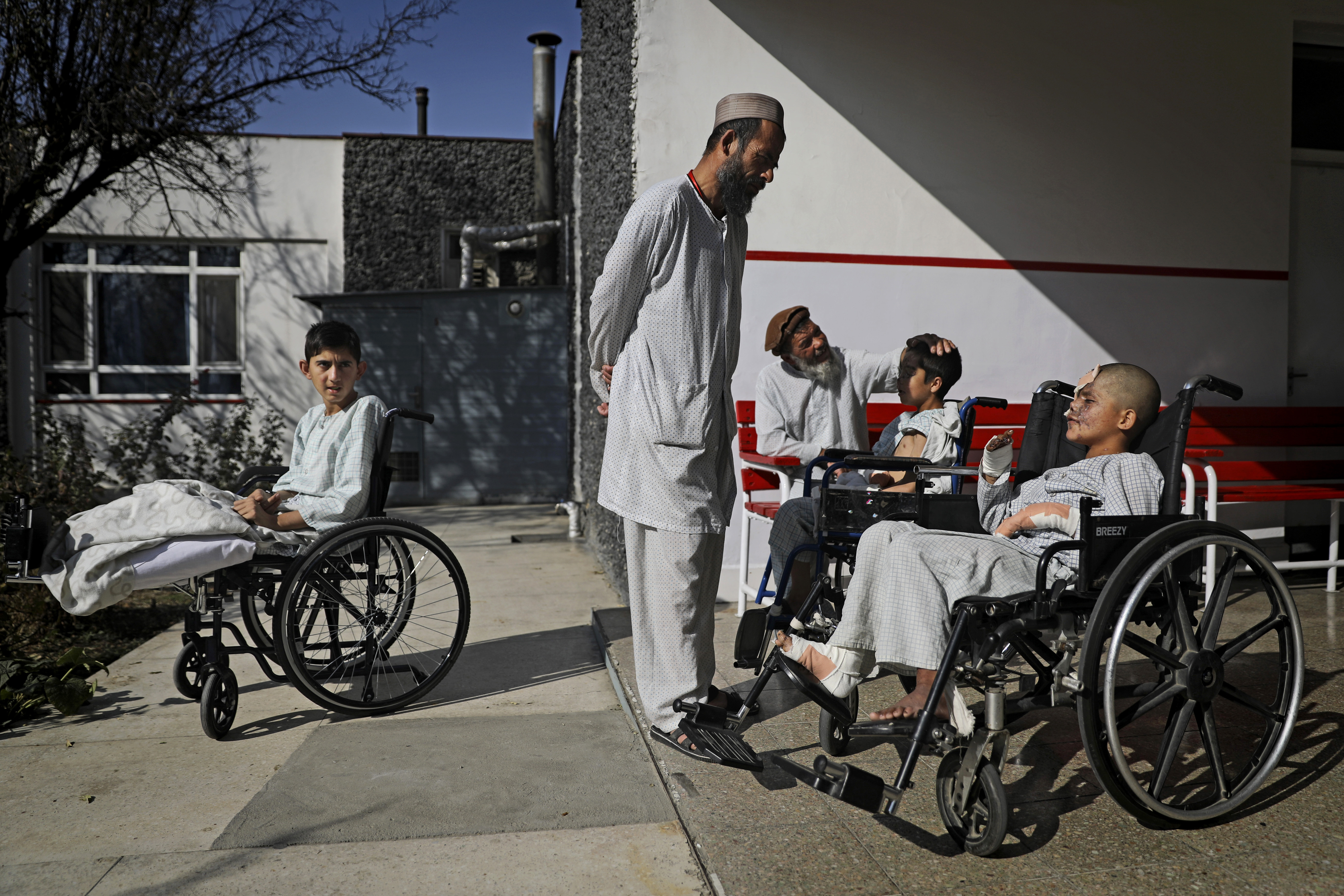 In this Thursday, Dec. 5, 2019, photo, young Afghan victims of war, Masiullah, left, who lost both his legs in a U.S. airstrike, nine-year-old Eimal, right, who has lost his right eye and several fingers on his hands in a landmine blast, and Ten-year-old Nessar Ahmad, second right, bask in sun outside their ward at Emergency Surgical Center for Civilian War Victims in Kabul, Afghanistan. The total number of children killed or maimed in more than four decades long Afghan war is not known. But, with a population where close to 50% are under the age of 20, the losses among the young is tremendous. (AP Photo/Altaf Qadri)