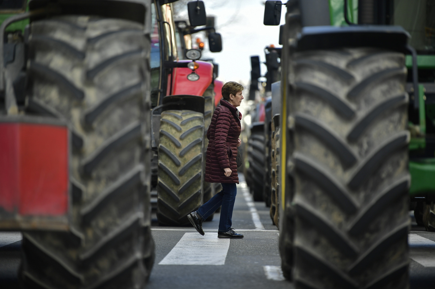 A pedestrian crosses a street as farmers block the center of the city with their tractors during a protest in Pamplona, northern Spain, Wednesday, Feb. 19, 2020. Farmers across Spain are taking part in mass protests over what they say are plummeting incomes for agricultural workers. (AP Photo/Alvaro Barrientos)