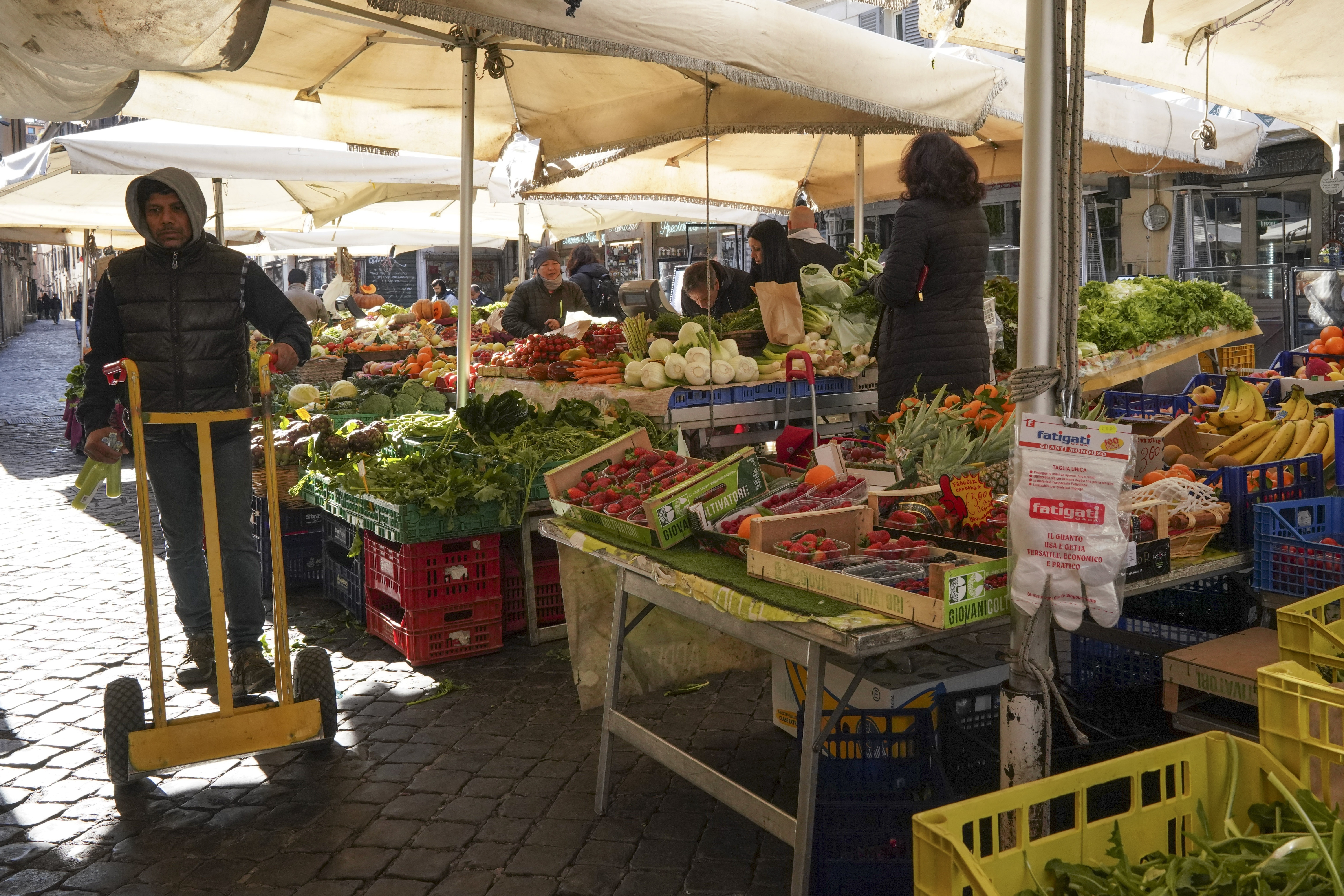 A man pushes a trolley as gloves hang at a fruit and vegetable stand at Campo dei Fiori open-air market, in Rome, Tuesday, March 10, 2020. The Italian government is assuring its citizens that supermarkets will remain open and stocked after panic buying erupted after broad anti-virus measures were announced nationwide, sparking overnight runs on 24-hour markets. (AP Photo/Andrew Medichini)
