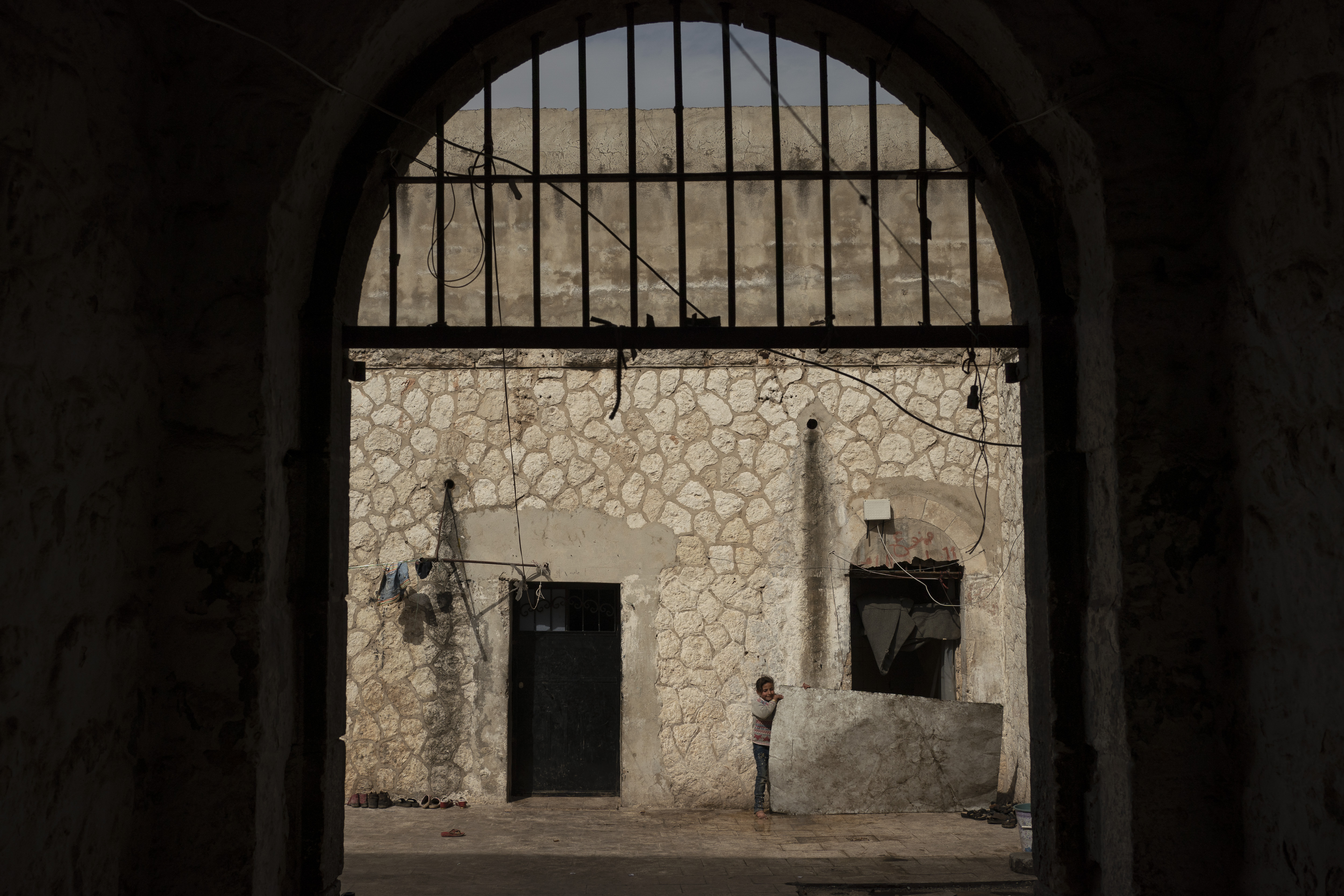 In this Thursday, March 12, 2020 photo, a girl stands inside Idlib's old central prison, now transformed into a camp for people displaced by fighting, in Idli, Syria. Idlib city is the last urban area still under opposition control in Syria, located in a shrinking rebel enclave in the northwestern province of the same name. Syria’s civil war, which entered its 10th year Monday, March 15, 2020, has shrunk in geographical scope -- focusing on this corner of the country -- but the misery wreaked by the conflict has not diminished. (AP Photo/Felipe Dana)