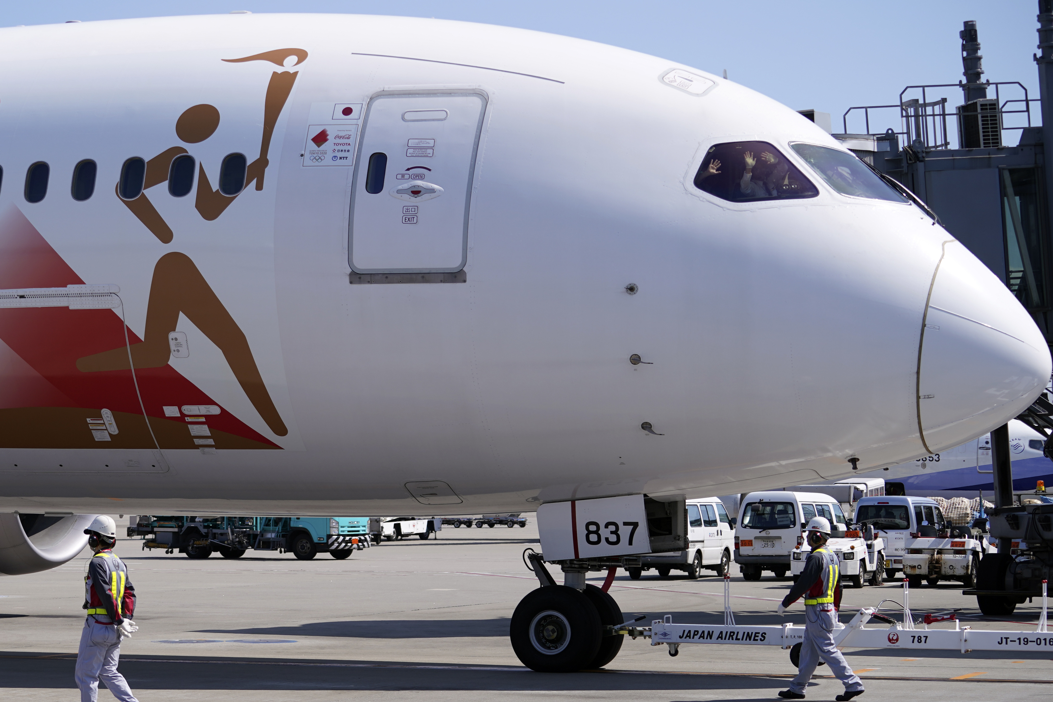 Pilots of the special "Tokyo 2020 Go" aircraft that will transport the Olympic Flame to Japan after the Torch Handover Ceremony in Greece, wave as they leave Haneda International Airport in Tokyo Wednesday, March 18, 2020. (AP Photo/Eugene Hoshiko)