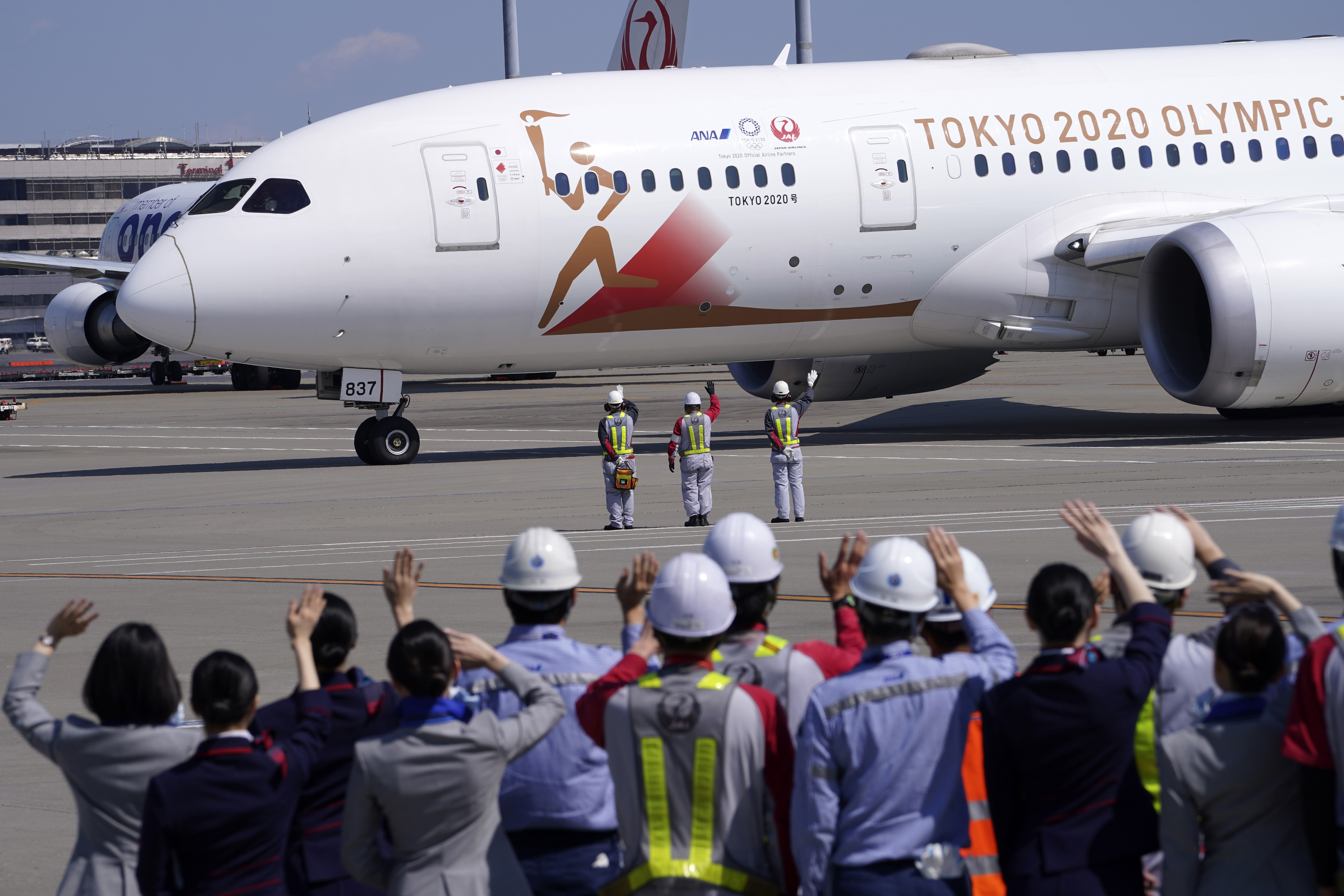 Ground crews of Japanese airlines wave to the special "Tokyo 2020 Go" aircraft that will transport the Olympic Flame to Japan from Greece, on its departure at Haneda International Airport in Tokyo Wednesday, March 18, 2020. (AP Photo/Eugene Hoshiko)