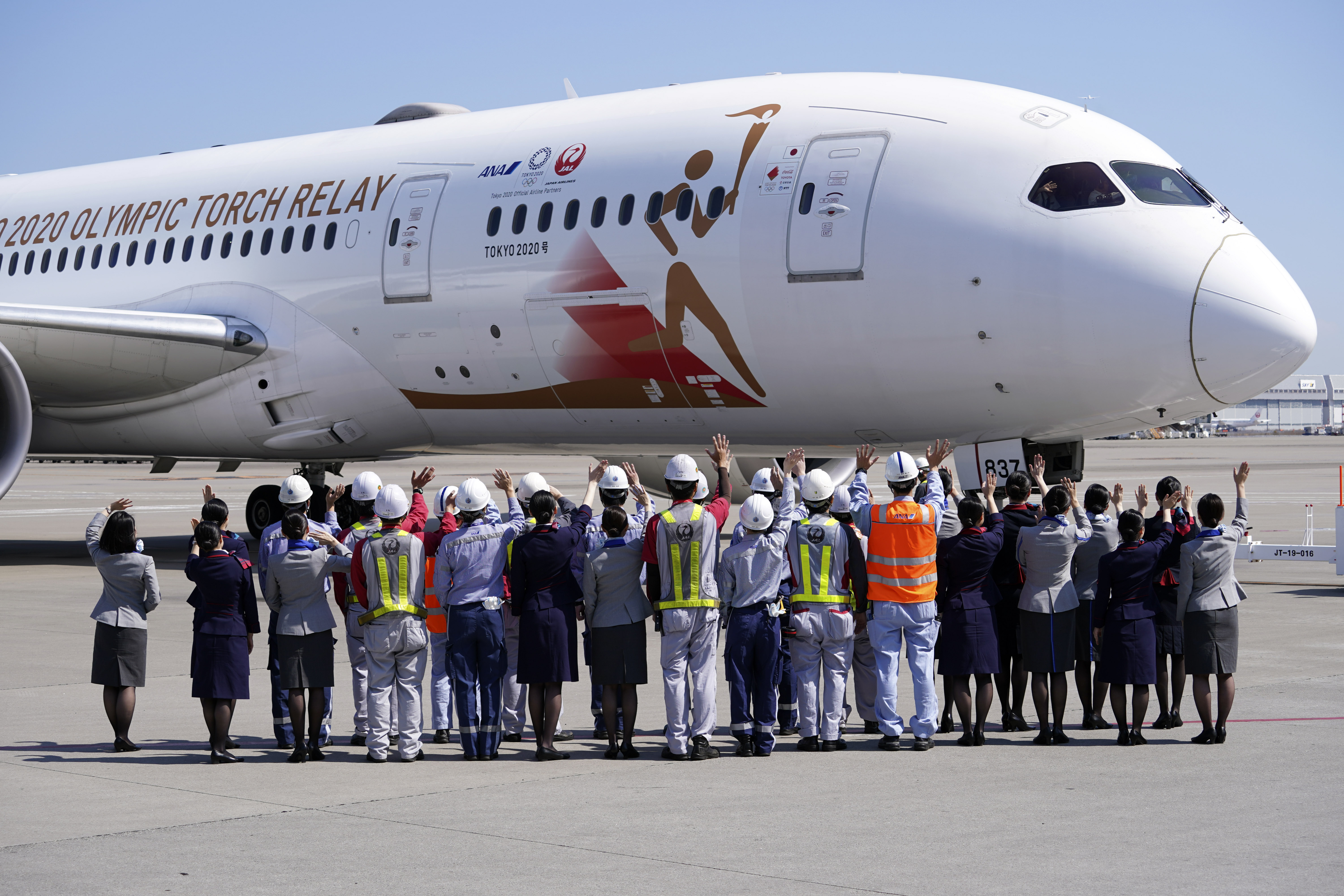 Ground crews of Japan Airlines wave to the special "Tokyo 2020 Go" aircraft that will transport the Olympic Flame to Japan after the Torch Handover Ceremony in Greece, departs at Haneda International Airport in Tokyo Wednesday, March 18, 2020. (AP Photo/Eugene Hoshiko)