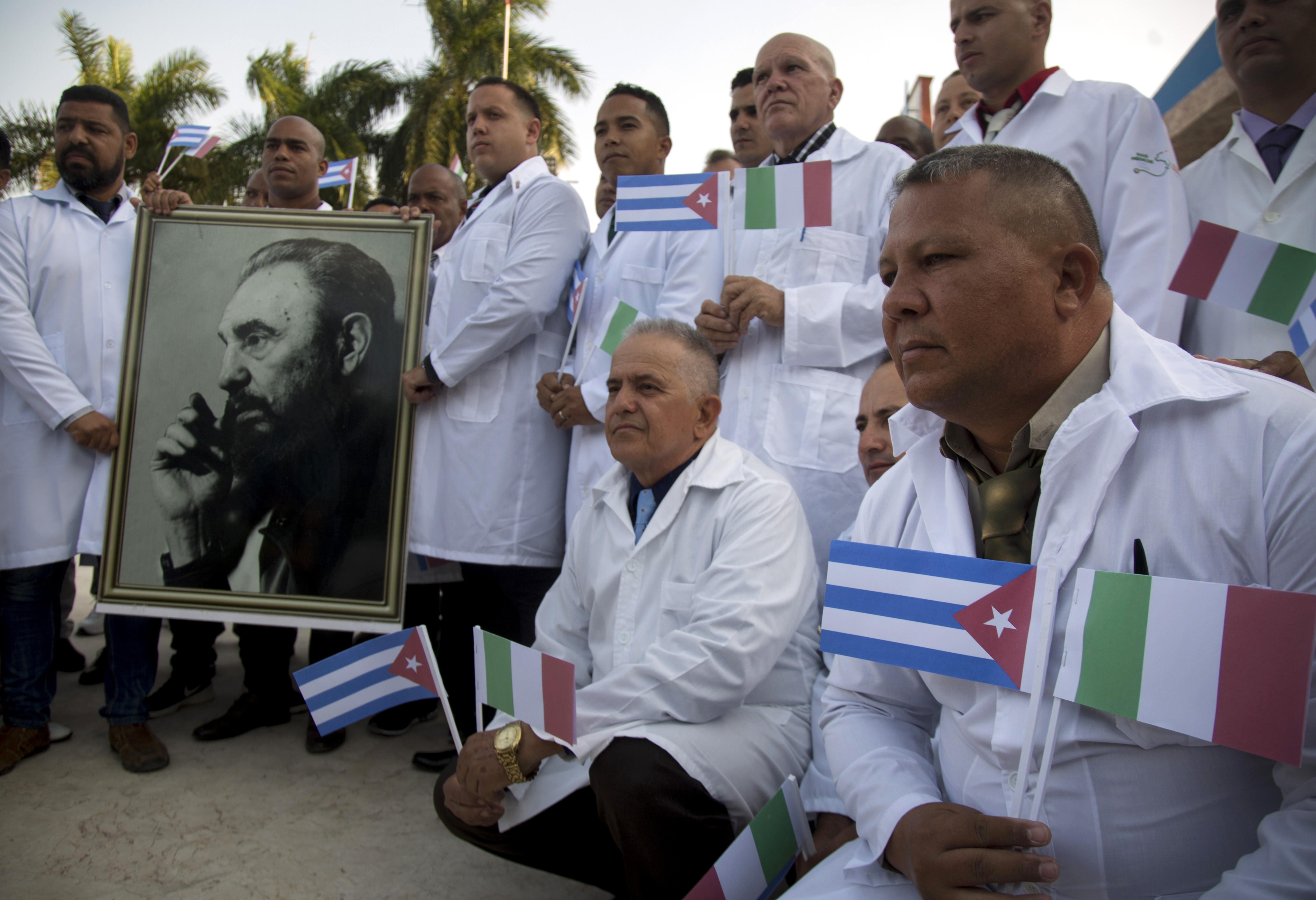 Several of the Cuban doctors and medical professionals that will depart for Italy to assist with the pandemic in the country pose for the media with a photo of Fidel Castro and flags of Italy and Cuba, in Havana, Cuba, Saturday, March 21, 2020. (AP Photo/Ismael Francisco)