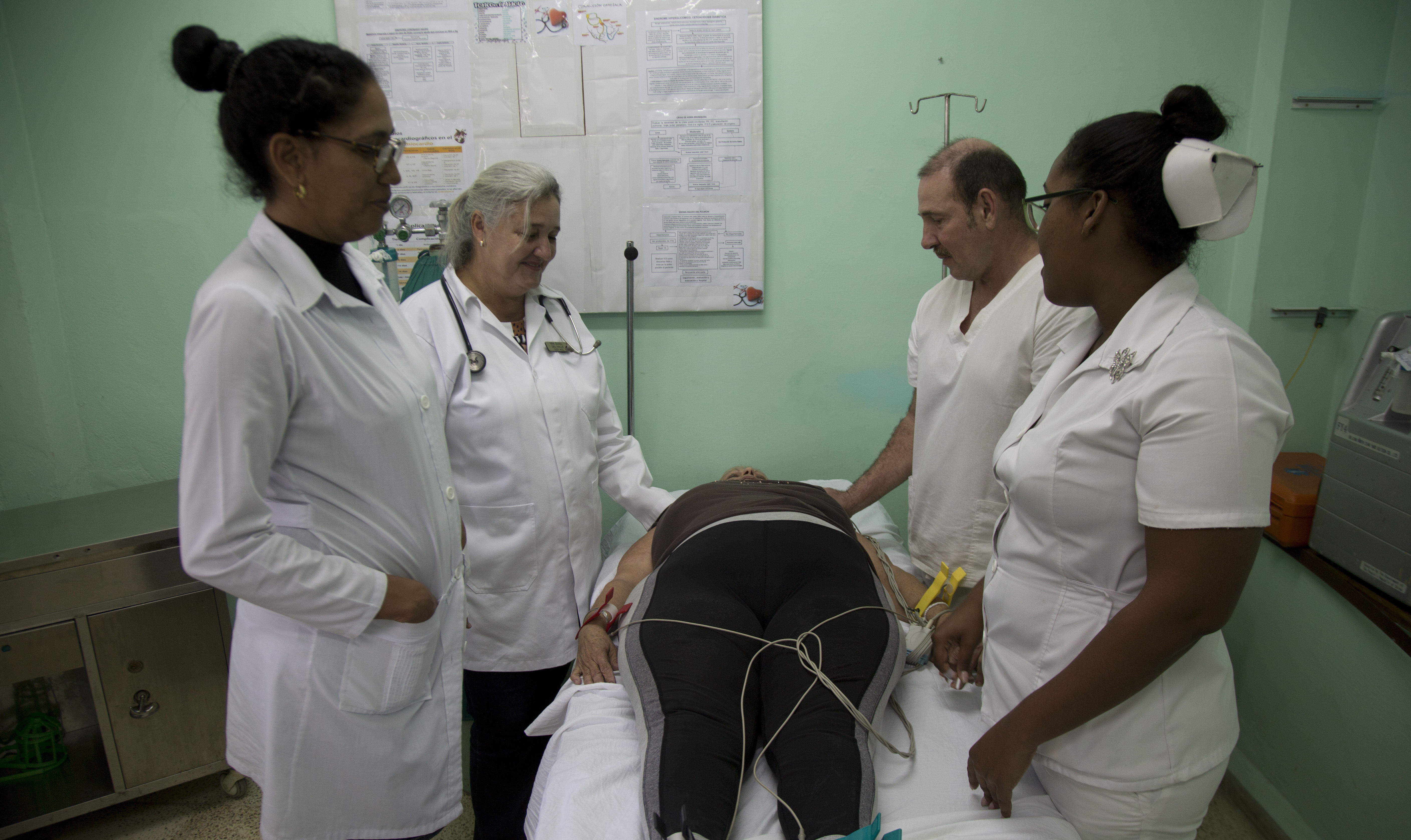 Nurses, technicians and specialists stand around a patient at a polyclinic in Havana, Cuba, Wednesday, Feb. 12, 2020.  Hundreds of neighborhood clinics are the front-line defense against contagious diseases in Cuba, providing care to patients seeking relief from colds, aches and minor injuries. (AP Photo/Ismael Francisco)