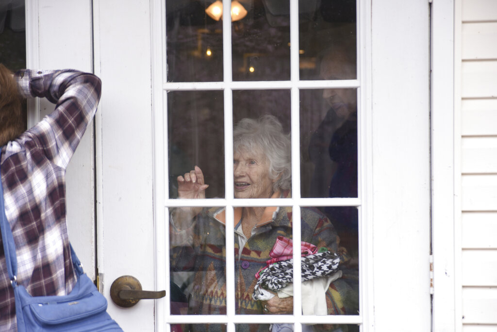 Under a cloudy sky on Thursday, March 26, 2020, a group of about 25 people, including members of the Alliance of Therapy Dogs and family members of residents, marched around Bright Leaf Senior Living, in Danville, Va., which has been closed to visitors for several weeks in an effort to curb the spread of COVID-19. Many of the social activities inside the facility have also been canceled, leaving the residents all but isolated in their rooms. The marchers smiled, waved, held up homemade signs and tried to talk to the residents inside, many of whom smiled and waved back and held up their own signs. (Caleb Ayers/Danville Register & Bee via AP)