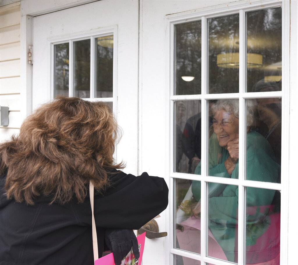 Under a cloudy sky on Thursday, March 26, 2020, a group of about 25 people, including members of the Alliance of Therapy Dogs and family members of residents, marched around Bright Leaf Senior Living, in Danville, Va., which has been closed to visitors for several weeks in an effort to curb the spread of COVID-19. Many of the social activities inside the facility have also been canceled, leaving the residents all but isolated in their rooms. The marchers smiled, waved, held up homemade signs and tried to talk to the residents inside, many of whom smiled and waved back and held up their own signs.  (Caleb Ayers/Danville Register & Bee via AP)