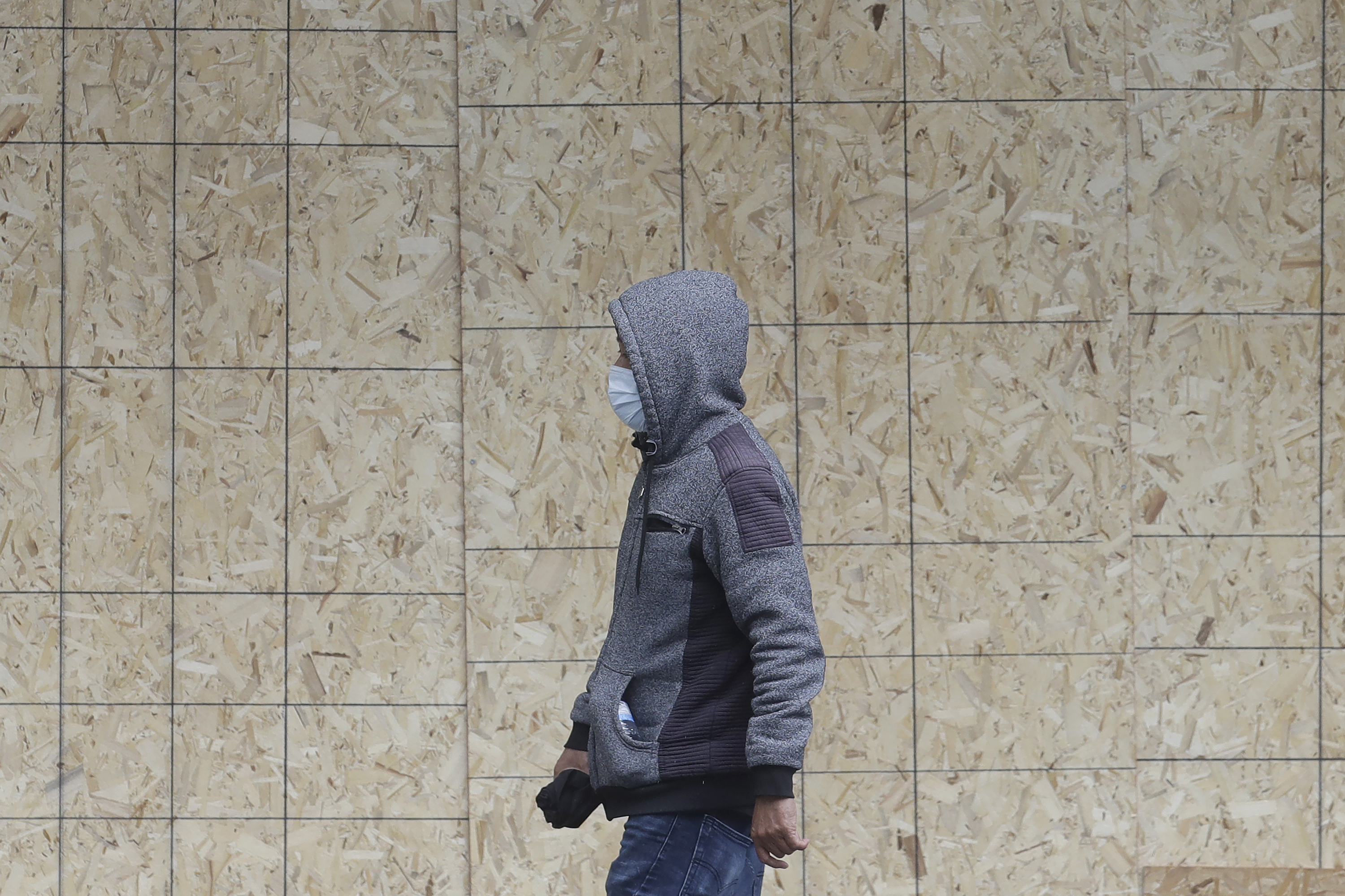 A man wears a mask while crossing in front of boarded up window to a Cole Haan store in San Francisco, Sunday, March 29, 2020. Californians endured a weekend of stepped-up restrictions aimed at keeping them home as much as possible while hospitals and health officials scrambled Sunday to ready themselves for a week that could see the feared dramatic surge in coronavirus cases. (AP Photo/Jeff Chiu)