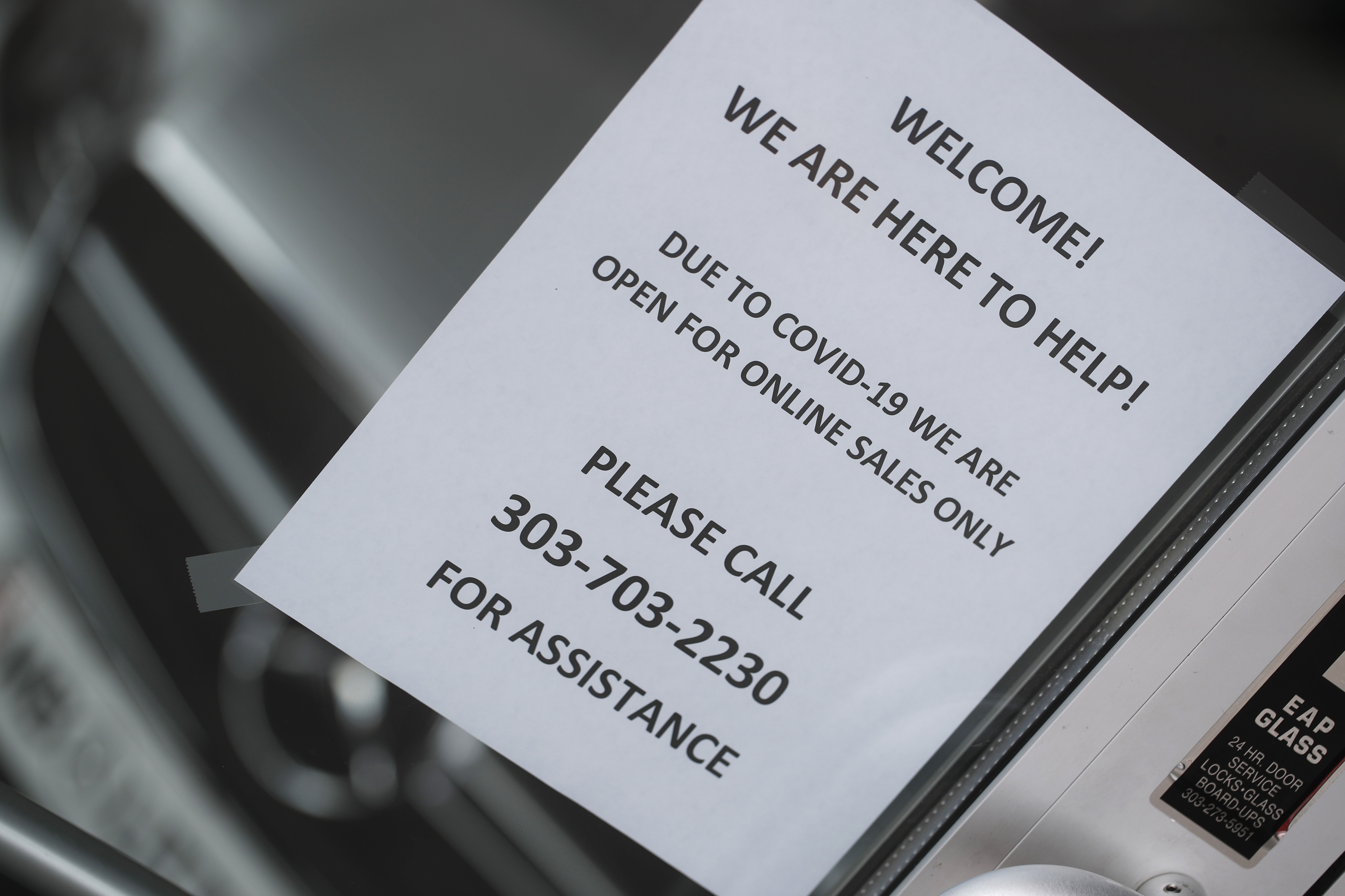 In this Sunday, April 5, 2020, photograph, a sign hangs in the front door of a Mercedes Benz dealership in Littleton, Colo. (AP Photo/David Zalubowski)