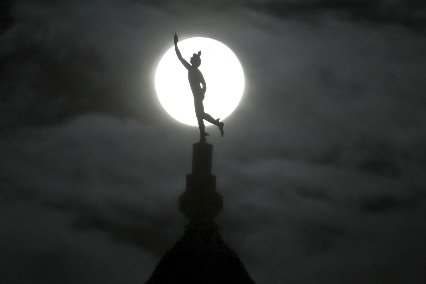 A supermoon rises behind a statue of the Roman god Mercury mounted on top of a hotel tower, Tuesday, April 7, 2020, in Nashville, Tenn. (AP Photo/Mark Humphrey)
