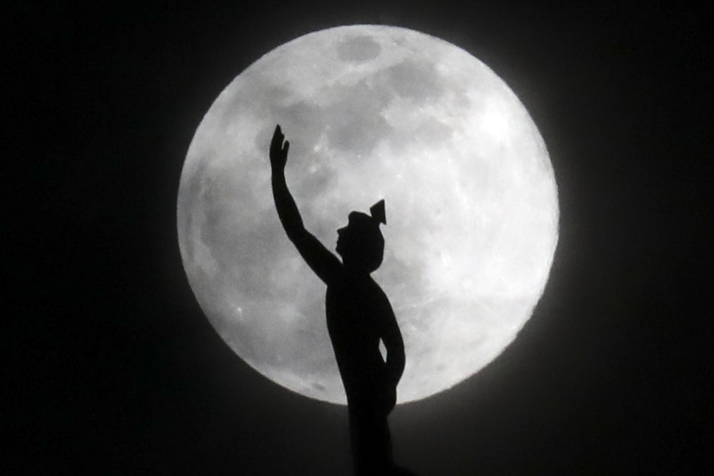 A supermoon rises behind a statue of the Roman god Mercury mounted on top of a hotel tower Tuesday, April 7, 2020, in Nashville, Tenn. (AP Photo/Mark Humphrey)