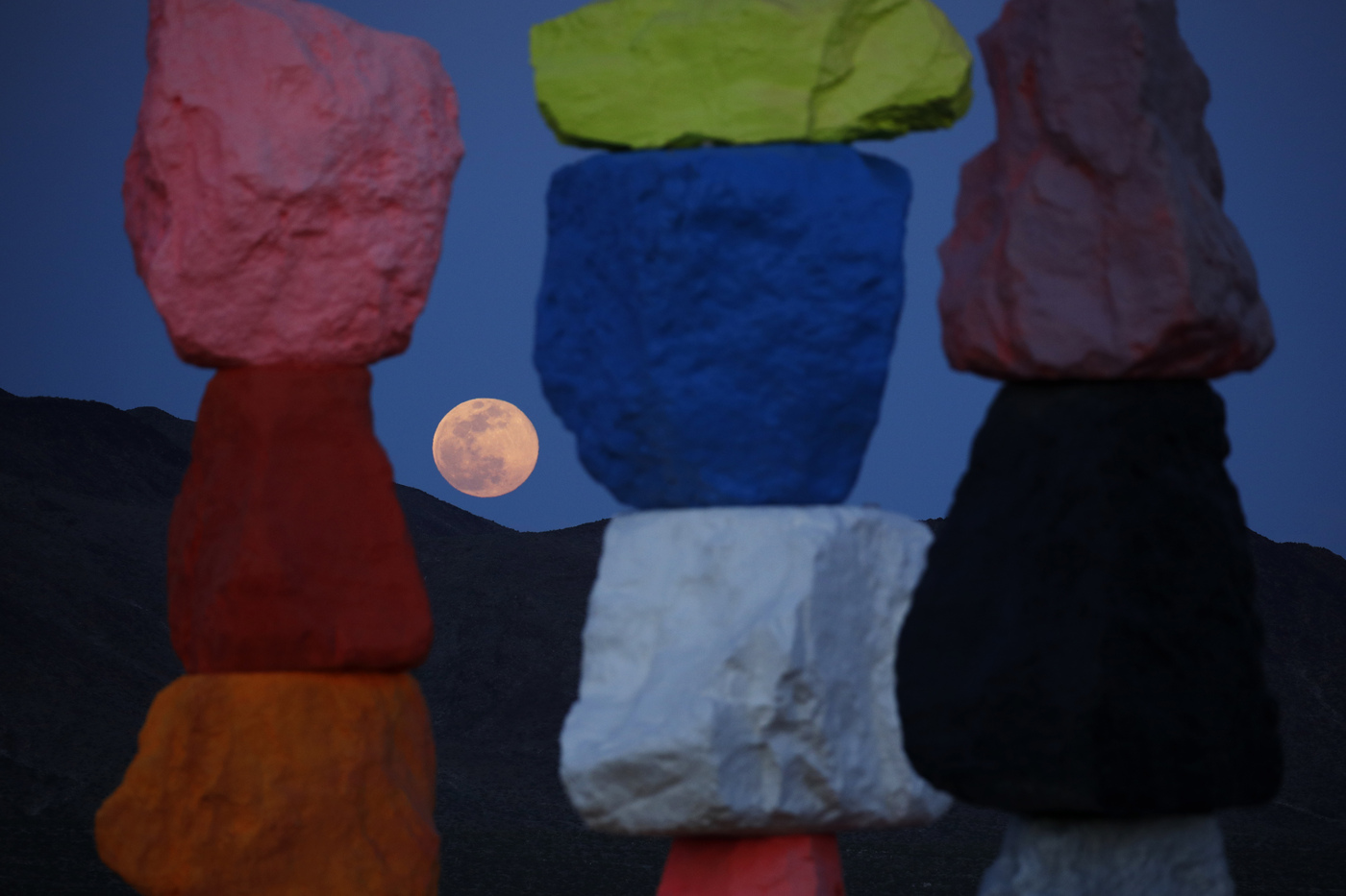 A supermoon rises behind the artwork titled Seven Magic Mountains by artist Ugo Rondinone, Tuesday, April 7, 2020, in Las Vegas. (AP Photo/John Locher)