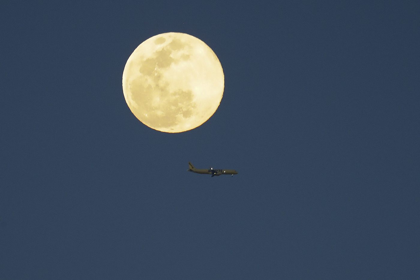 An airplane flys past a super moon as it rises in the sky Tuesday, April 7, 2020, in Orlando, Fla. (AP Photo/John Raoux)