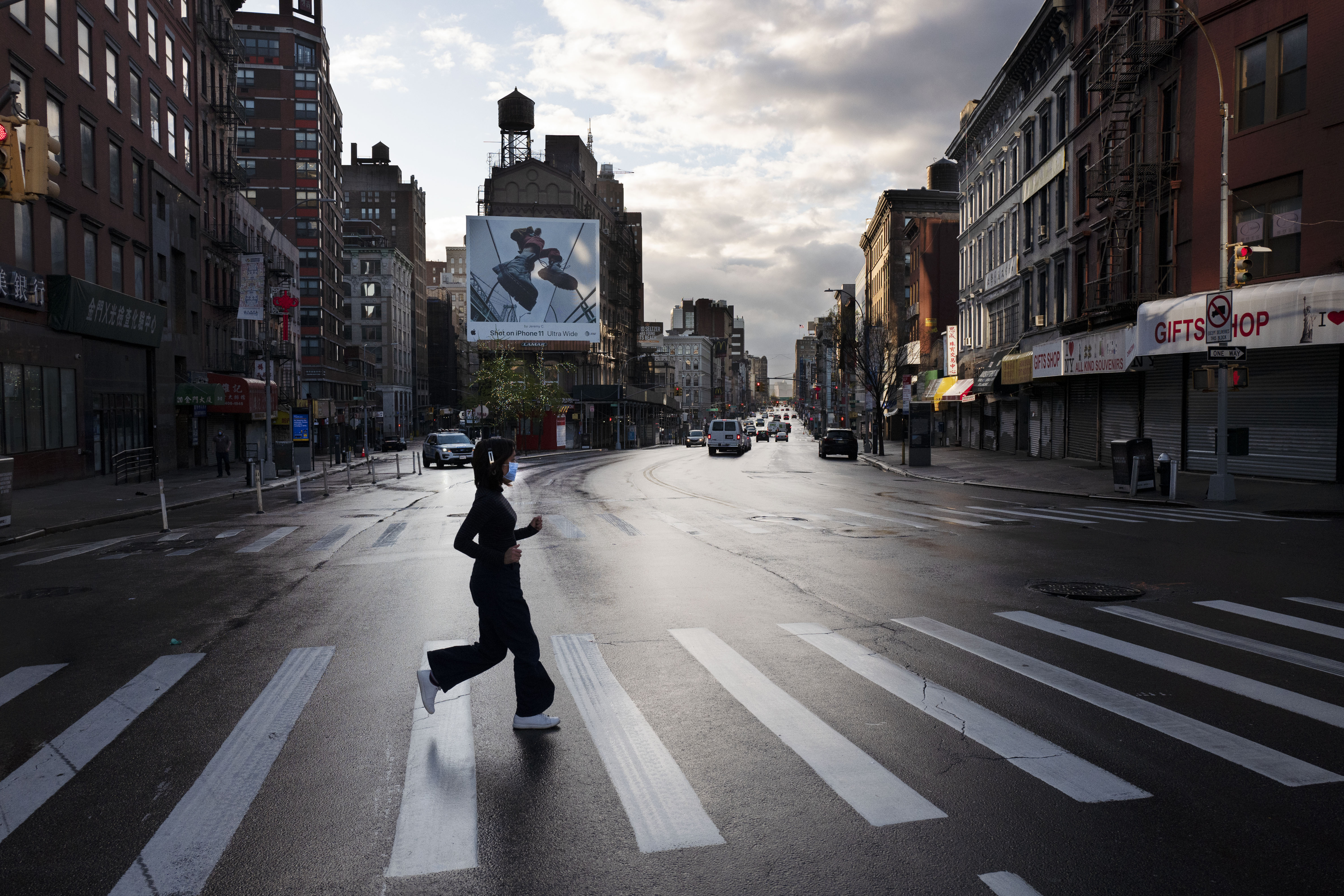 A woman wearing a mask jogs across a quiet section of Canal Street during the coronavirus pandemic Monday, April 13, 2020, in New York. Canal Street is normally packed with bumper-to-bumper traffic and pedestrians during the evening rush hour. (AP Photo/Mark Lennihan)
