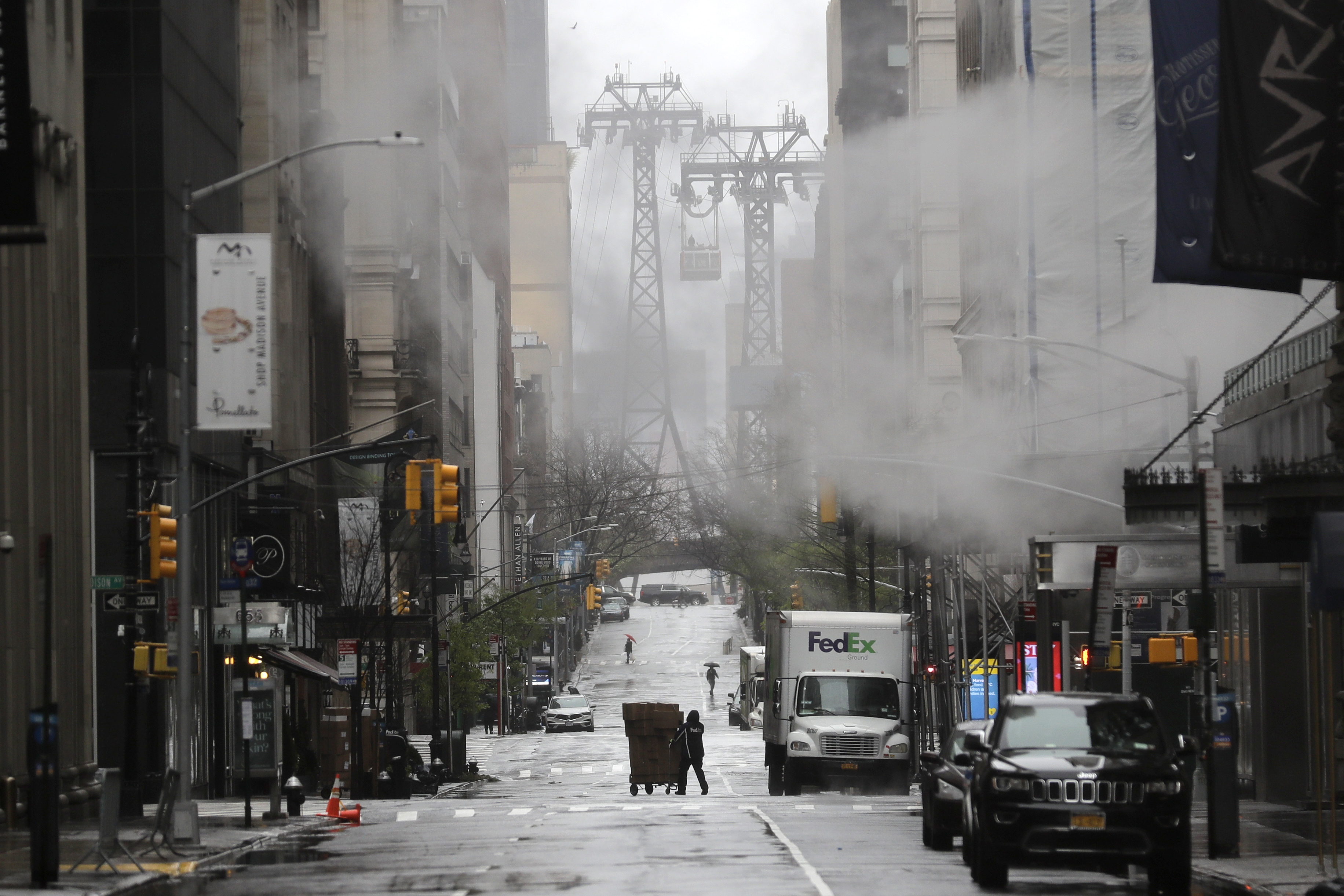 A FedEx delivery man rolls his packages across a quiet street on a rainy day in New York, Monday, April 13, 2020. Gov. Andrew Cuomo says New York's death toll from coronavirus has topped 10,000, with hospitals still seeing 2,000 new patients a day. The death tally hit the milestone only about a month after the state recorded its first death. (AP Photo/Seth Wenig)