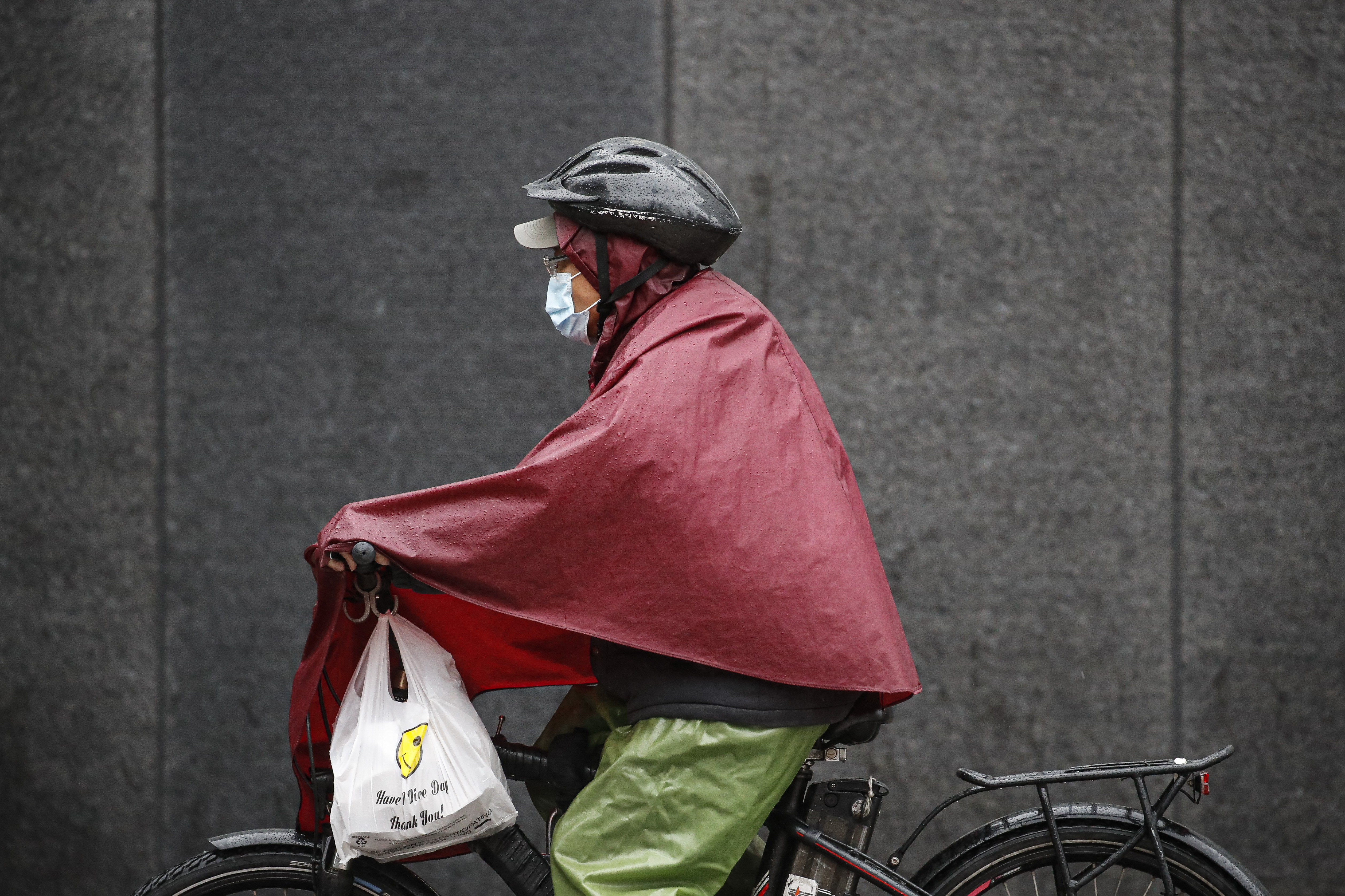 A delivery worker wears personal protective equipment due to COVID-19 concerns while riding a bicycle through the rain outside NYU Langone Medical Center, Monday, April 13, 2020, in New York. The new coronavirus causes mild or moderate symptoms for most people, but for some, especially older adults and people with existing health problems, it can cause more severe illness or death. (AP Photo/John Minchillo)