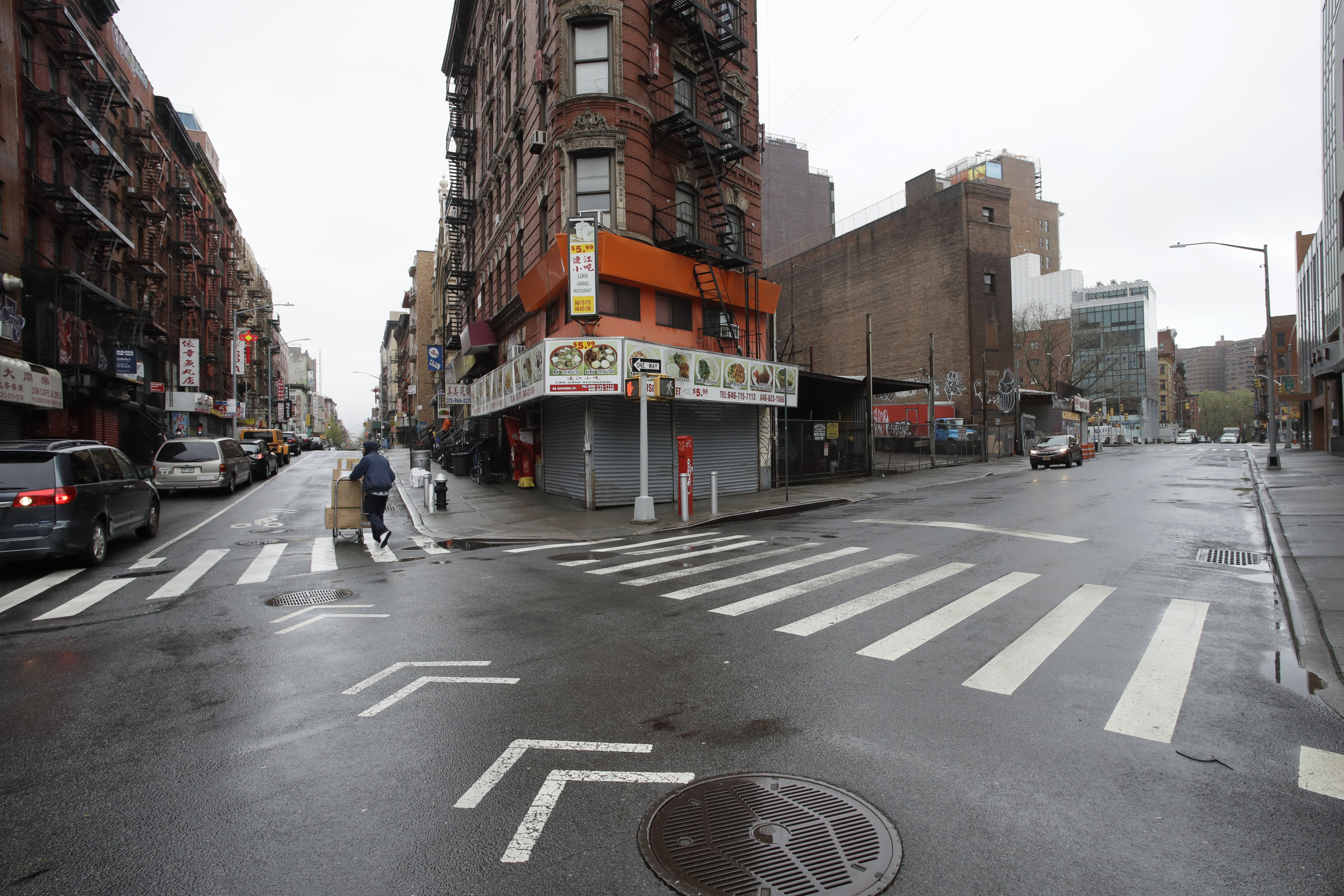 A man pushes a cart of boxes through the intersection of Eldridge St. and Division Street, Monday, April 13, 2020 in New York's Chinatown during the coronavirus pandemic. The streets are normally bustling with vehicles and pedestrians. (AP Photo/Mark Lennihan)