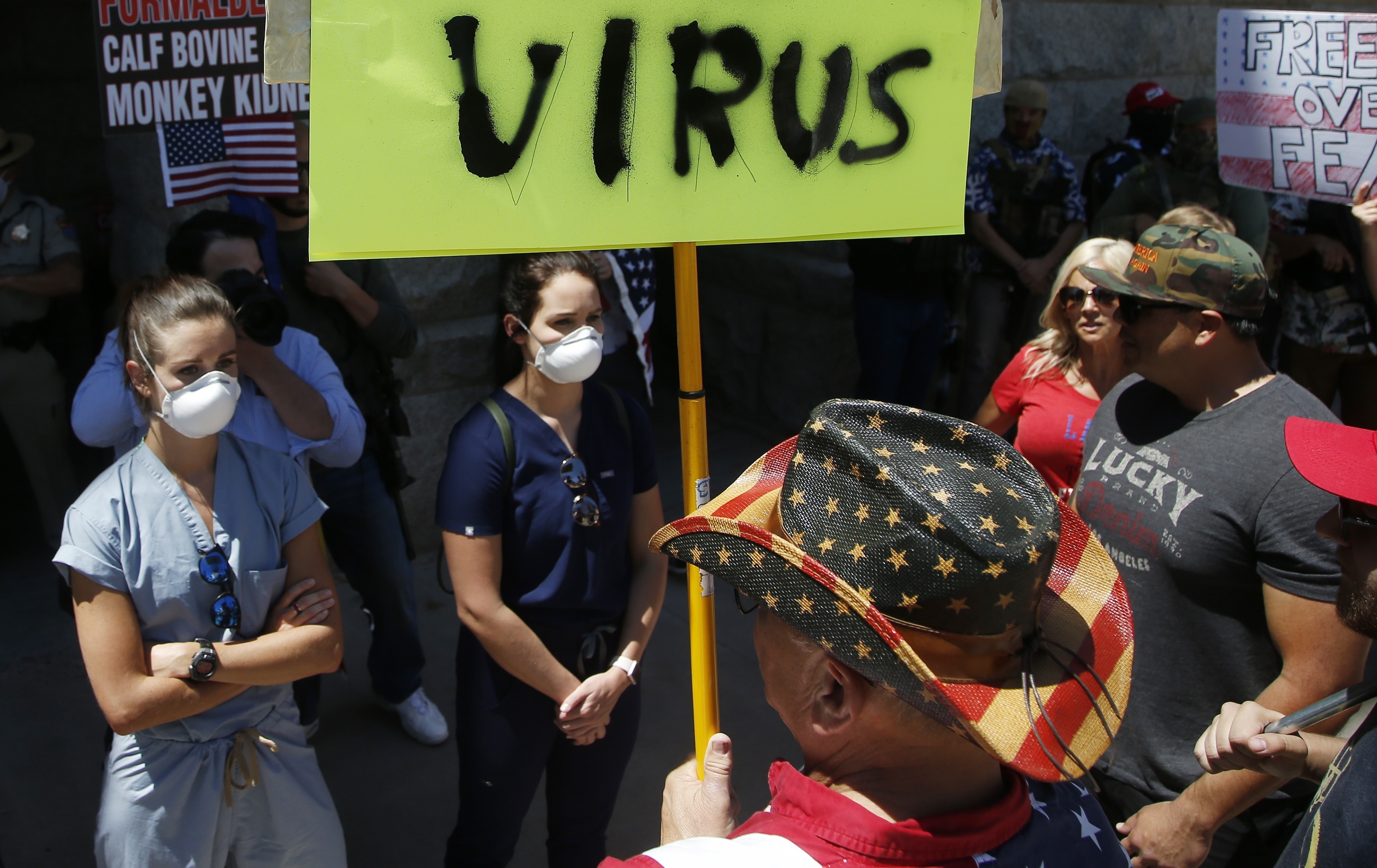 Caregivers stand in front of protesters at the main entrance to the Arizona Capitol at a rally to 're-open' Arizona against the governor's stay-at-home order due to the coronavirus Monday, April 20, 2020, in Phoenix. (AP Photo/Ross D. Franklin)