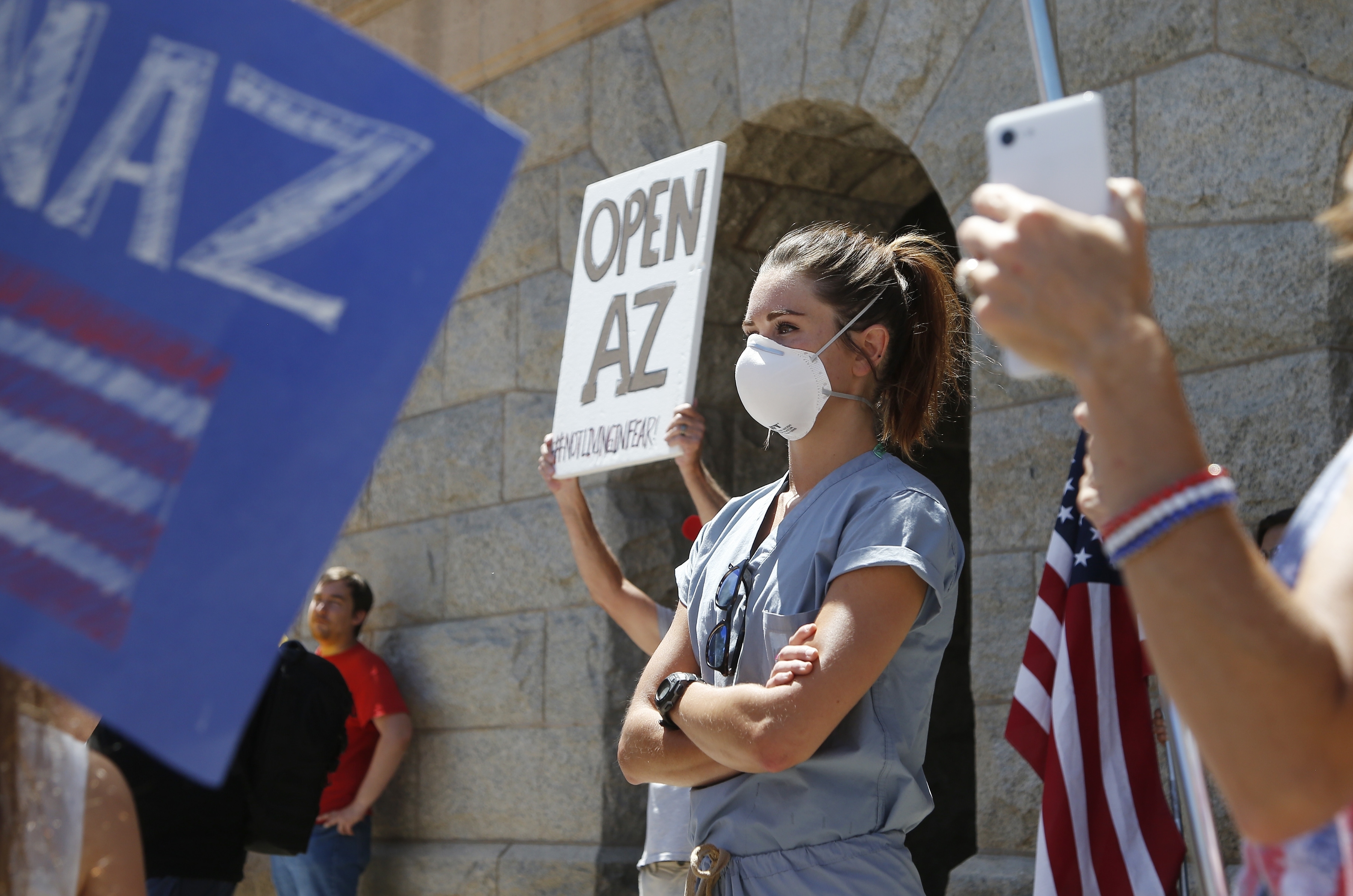 A caregiver stands in front of the Arizona Capitol as protesters surround her at a rally to 're-open' Arizona against the governor's stay-at-home order due to the coronavirus Monday, April 20, 2020, in Phoenix. (AP Photo/Ross D. Franklin)