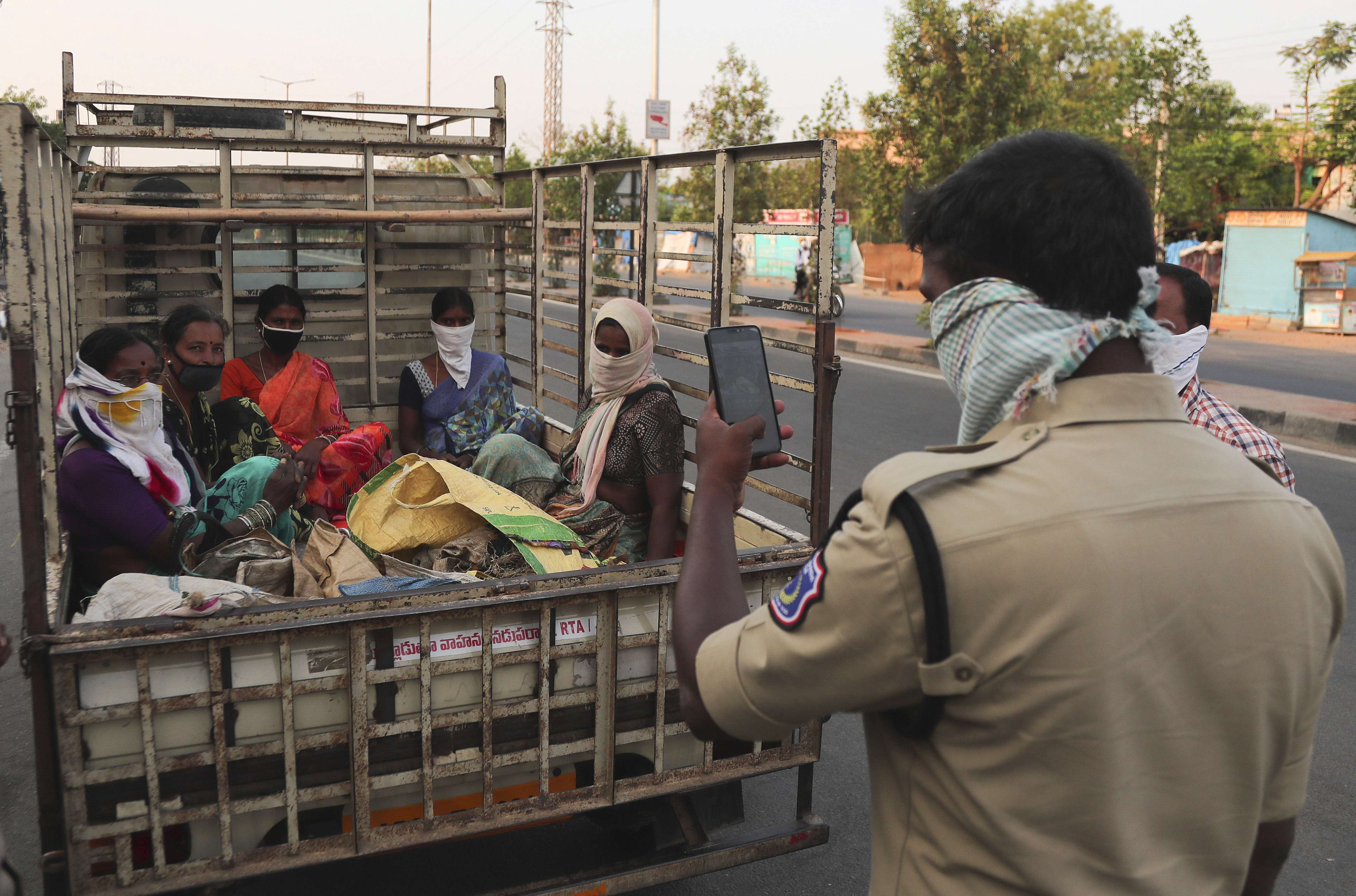 An Indian policeman takes photograph of women traveling in a mini lorry violating rules during lockdown to prevent the spread of new coronavirus in Hyderabad, India, Wednesday, April 22, 2020. India has reported nearly 20,000 confirmed cases of COVID-19 and over 600 deaths. (AP Photo/Mahesh Kumar A.)