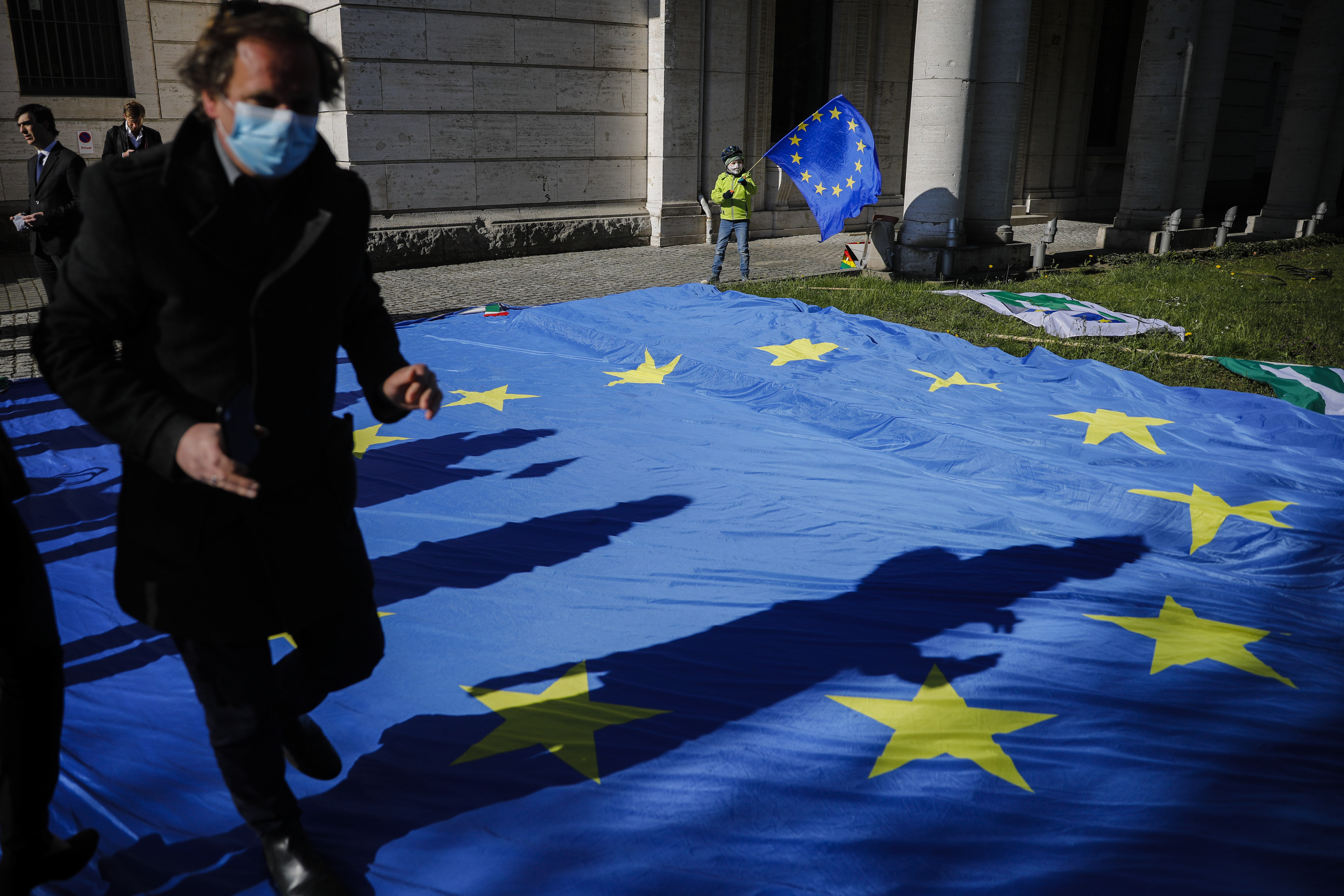 A man with a face mask and a child with an European flag attend an event of the Pulse of Europe movement to collecting signatures for more support for Italy during the coronavirus and the COVID-19 outbreak in front of the Italian embassy in Berlin, Germany, Wednesday, April 22, 2020. (AP Photo/Markus Schreiber)
