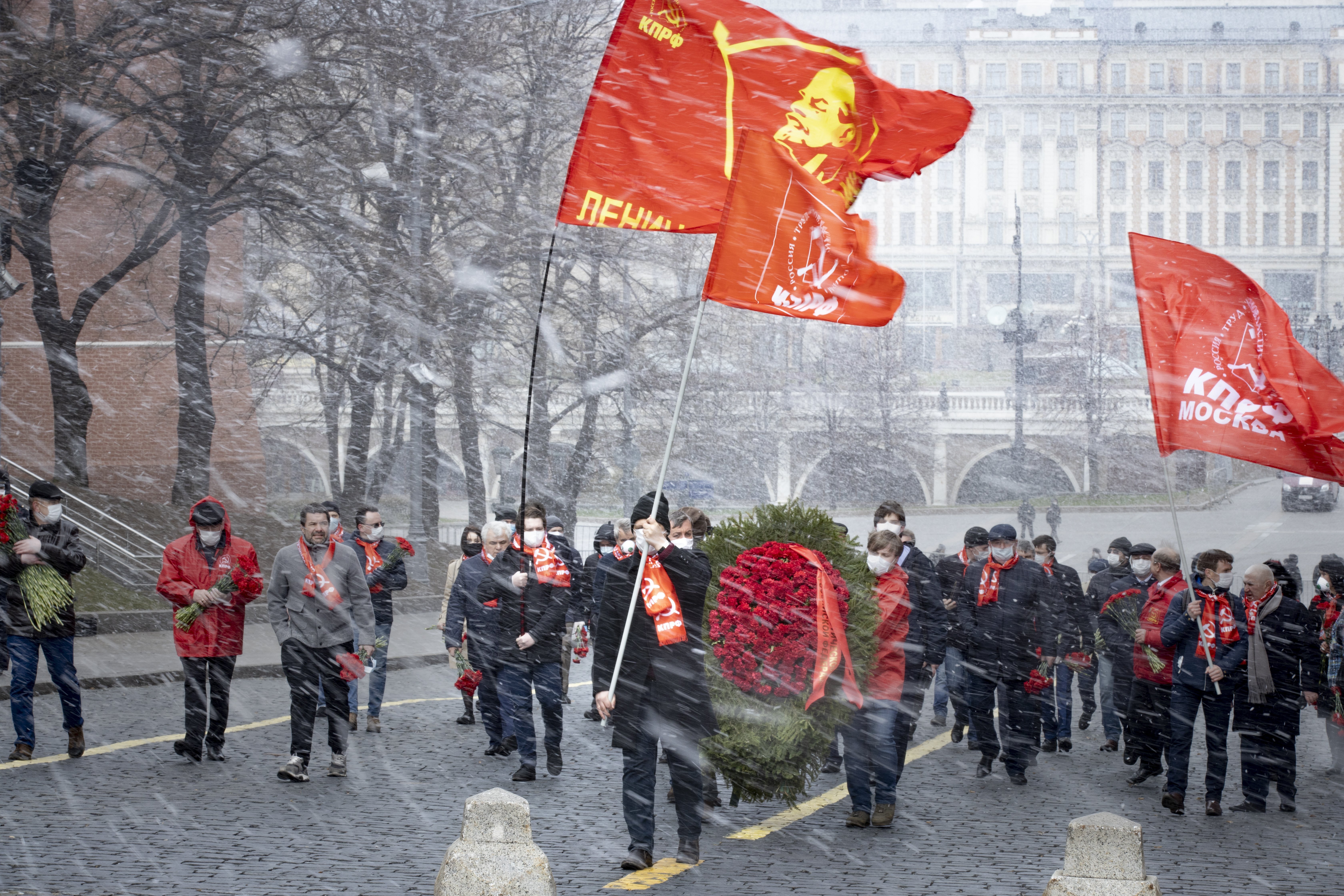 Russian communists and supporters, some of them wearing face masks to protect against coronavirus, observe social distancing guidelines as they walk under a snowfall to visit the Mausoleum of the Soviet founder Vladimir Lenin to mark the 150th anniversary of his birth, at Moscow's Red Square during a snowfall in Moscow, Russia, Wednesday, April 22, 2020. Russia's Communist Party traditionally marks the birthday of Soviet founder Vlaimir Lenin every year. This year was no exception, even though Muscovites are currently not allowed to leave their homes unless for work, grocery shopping, visiting a doctor or taking out the trash. (AP Photo/Alexander Zemlianichenko)