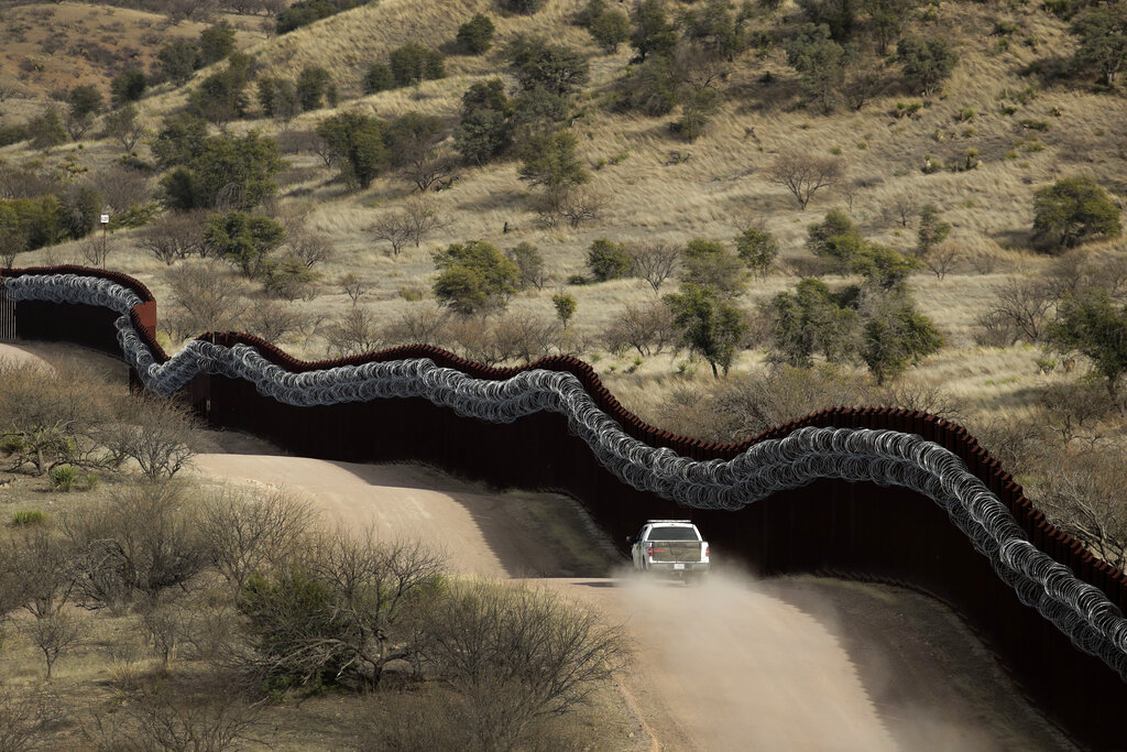 FILE - This March 2, 2019, file photo, shows a Customs and Border Control agent patrolling on the US side of a razor-wire-covered border wall along the Mexico east of Nogales, Ariz. Border activist Scott Warren will be retried after a jury was unable to reach a verdict on charges related to aiding migrants near Arizona's border with Mexico, U.S. prosecutors said Tuesday, July 2, 2019. (AP Photo/Charlie Riedel, File)