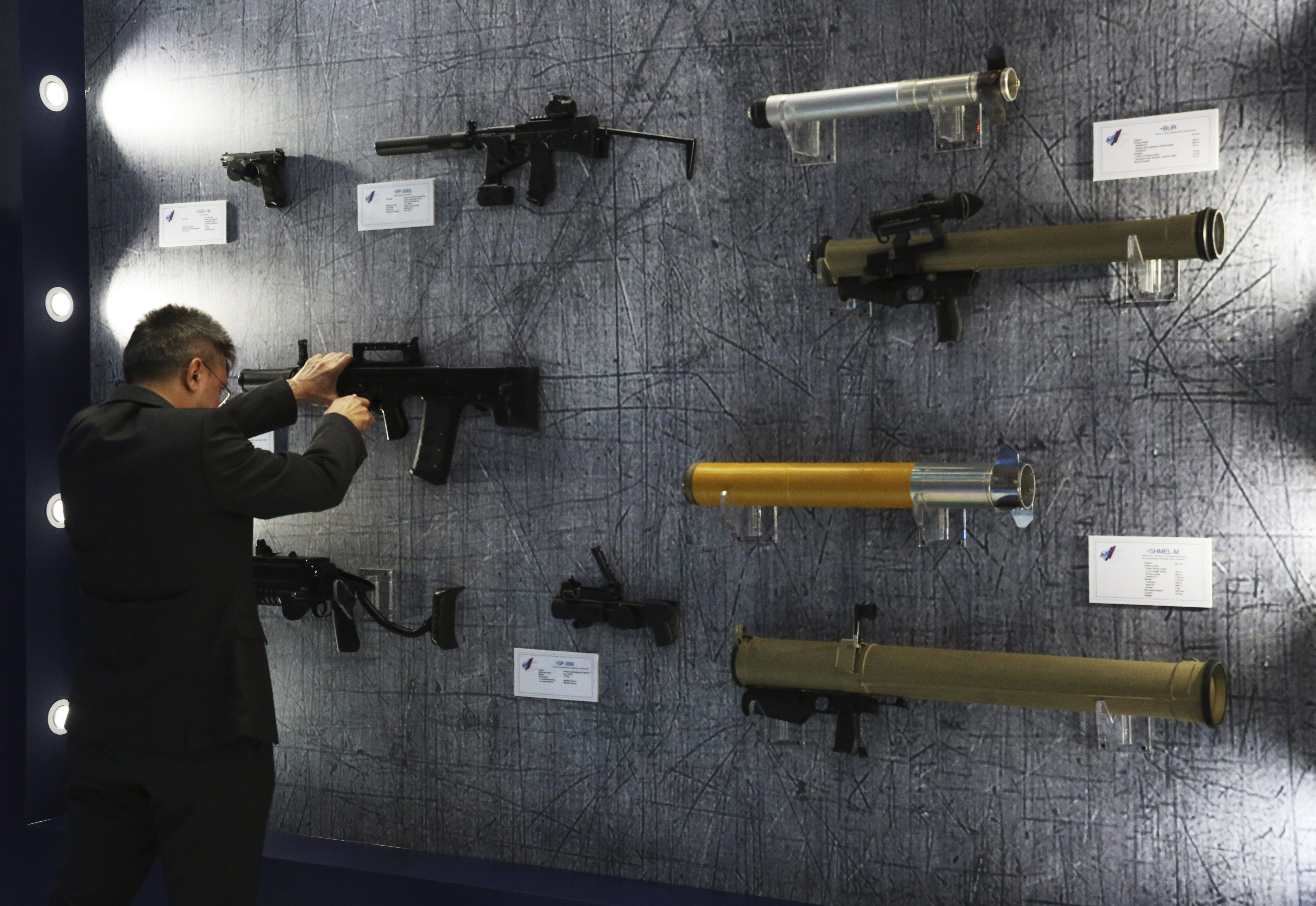 A passerby struggles to put an assault rifle back on the wall at a display at the International Defense Exhibition and Conference in Abu Dhabi, United Arab Emirates, Sunday, Feb. 17, 2019. The biennial arms show in Abu Dhabi comes as the United Arab Emirates faces increasing criticism for its role in the yearlong war in Yemen. (AP Photo/Jon Gambrell)