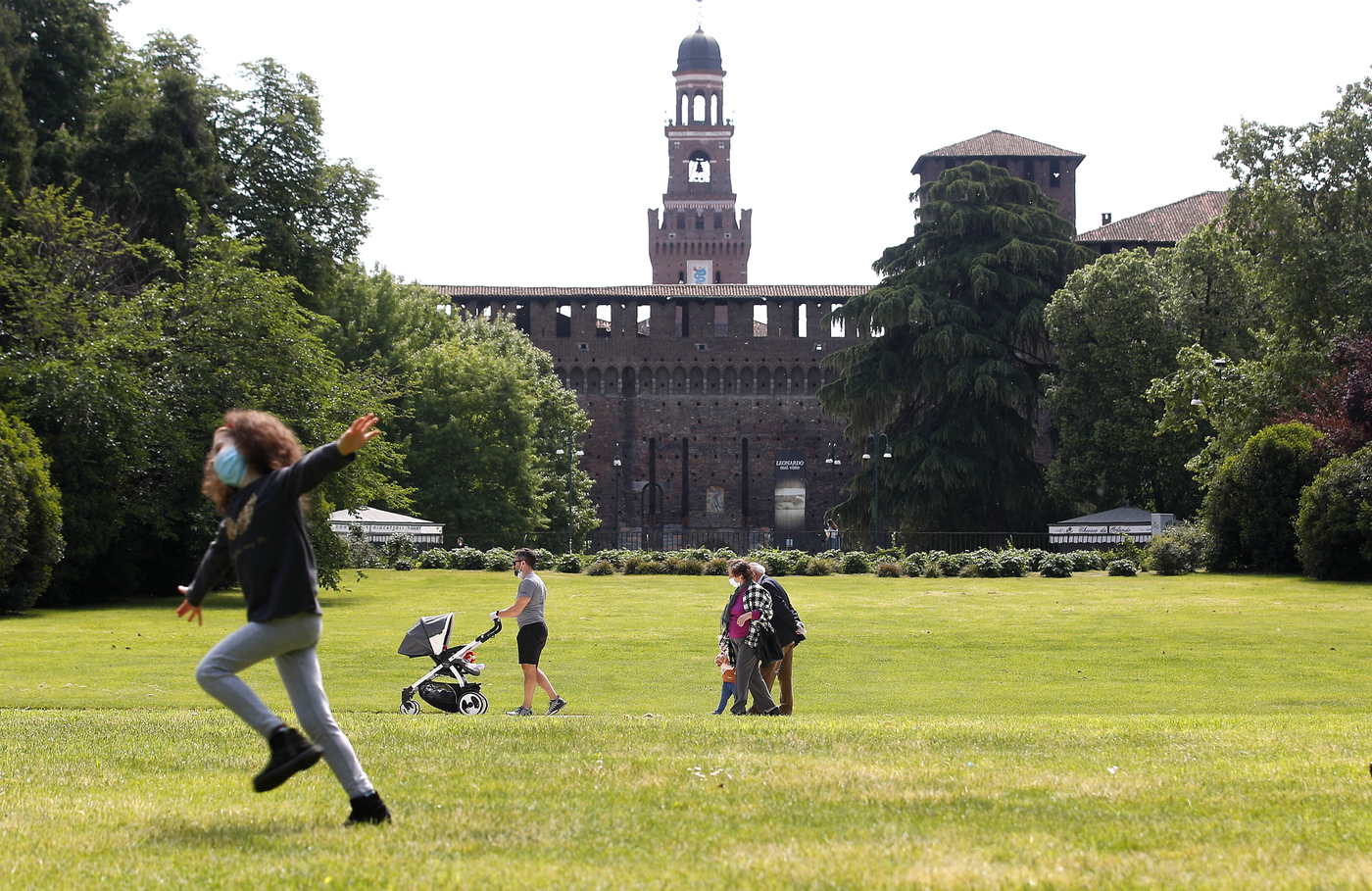 A girl wearing a mask runs as people stroll in a park which reopened after several weeks of closure, in Milan, Italy, Monday, May 4, 2020. Italy began stirring again Monday after a two-month coronavirus shutdown, with 4.4 million Italians able to return to work and restrictions on movement eased in the first European country to lock down in a bid to stem COVID-19 infections.  (AP Photo/Antonio Calanni)