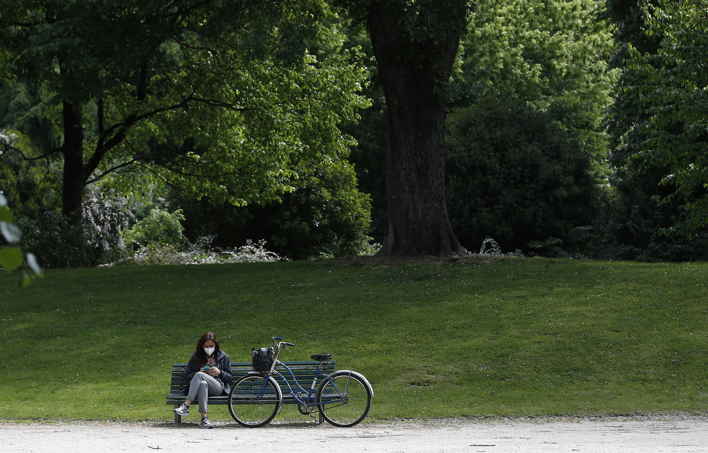 A woman sits by her bike on a bench in a park which reopened after several weeks of closure, in Milan, Italy, Monday, May 4, 2020. Italy began stirring again Monday after a two-month coronavirus shutdown, with 4.4 million Italians able to return to work and restrictions on movement eased in the first European country to lock down in a bid to stem COVID-19 infections.  (AP Photo/Antonio Calanni)