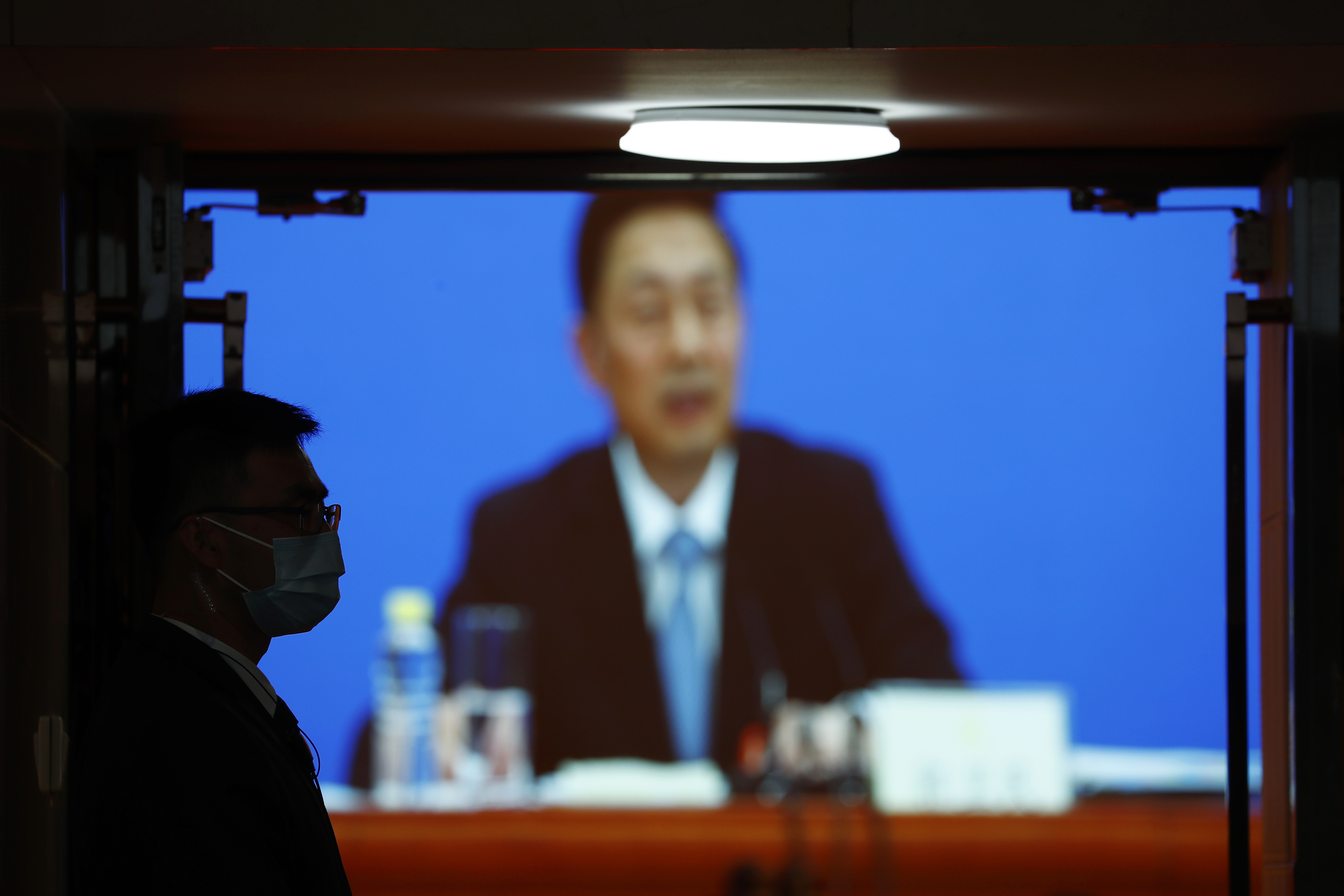 A security guard, left, stands guard outside a room where a news conference by Guo Weimin, spokesman for the National Committee of the Chinese People's Political Consultative Conference (CPPCC), is broadcasted, at a media center in Beijing, China Wednesday, May 20, 2020. This year’s version of the National People’s Congress — China’s biggest political meeting of the year — will be unlike any other. Delayed from March because of the then-spiraling coronavirus outbreak, the decision to go ahead with the annual gathering starting Friday signals a partial return to normalcy in the country where the pandemic first broke out. (Thomas Peter/Pool Photo via AP)