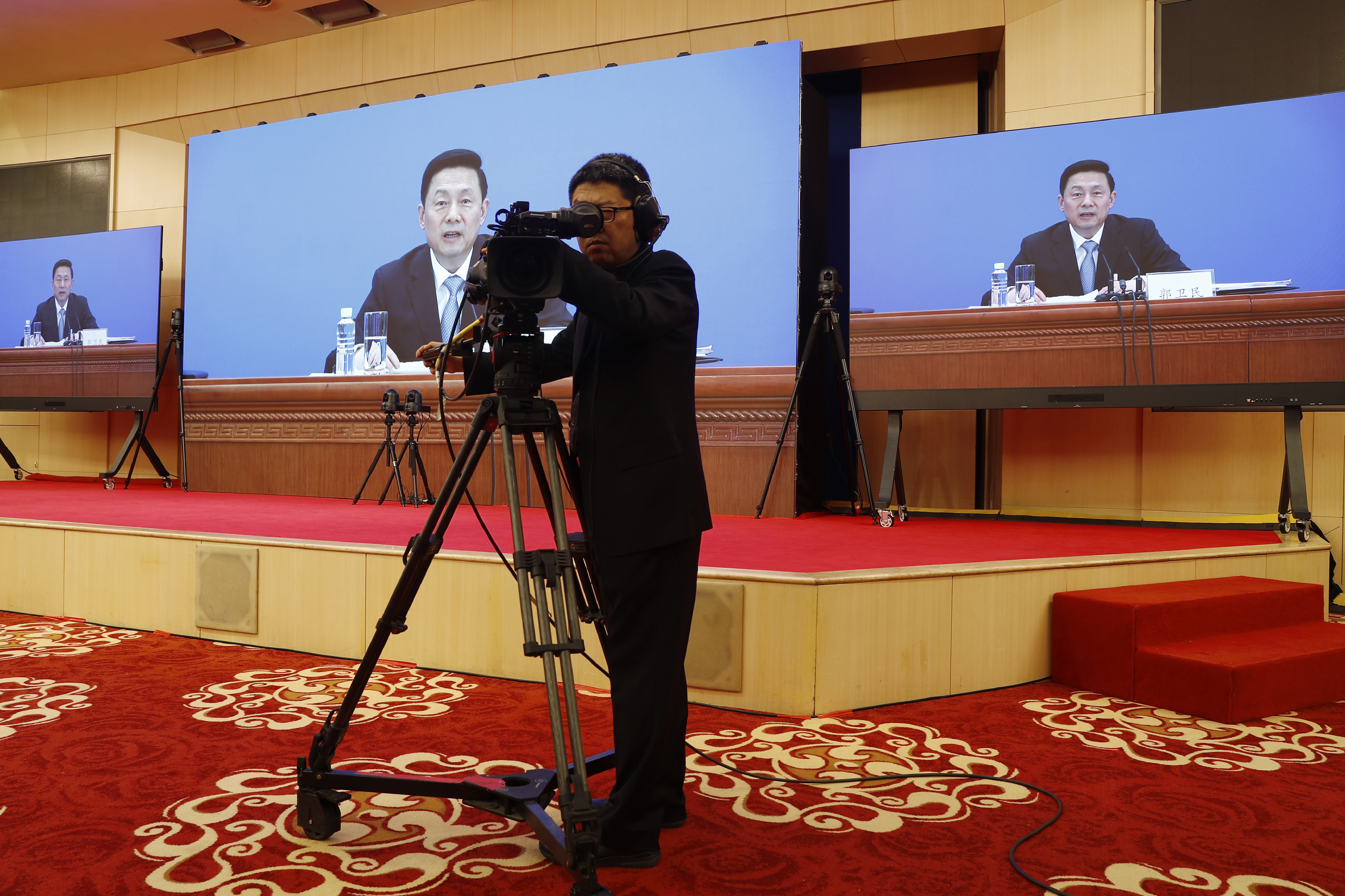 Guo Weimin, spokesman for the National Committee of the Chinese People's Political Consultative Conference (CPPCC), is seen on screens during a news conference broadcasted at a media center in Beijing, Wednesday, May 20, 2020. (Thomas Peter/Pool Photo via AP)