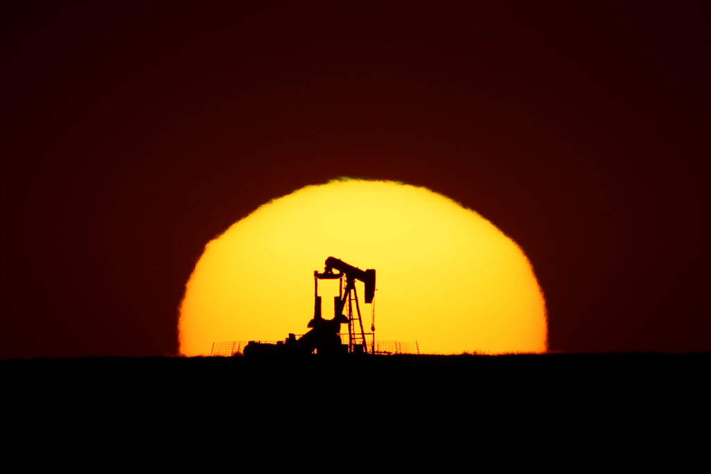 An idle oil pumping unit is silhouetted against the setting sun, Wednesday, May 20, 2020, in a field south of Oakley, Kan. Surplus global oil production coupled with reduced demand as people stay home because of coronavirus restrictions have led to the lowest oil prices in decades which have only recently started to rebound somewhat. (AP Photo/Charlie Riedel)