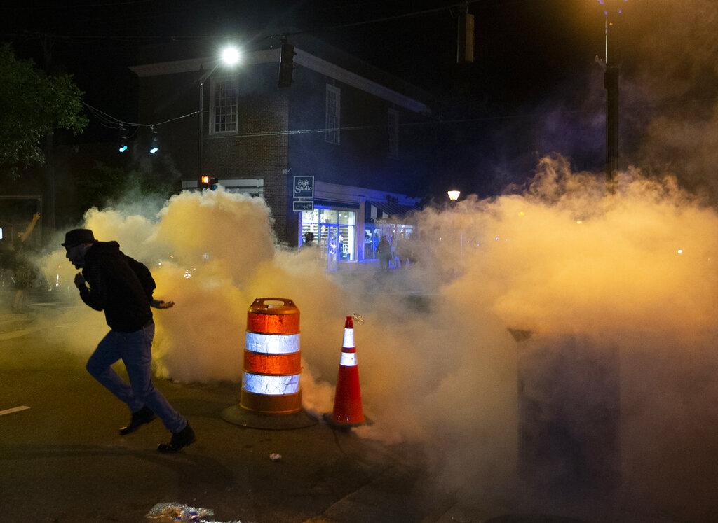 A protester runs after placing a construction barrel on top of a gas grenade in downtown Fredericksburg, Va. on Sunday, May 31, 2020. (Mike Morones/The Free Lance-Star via AP)