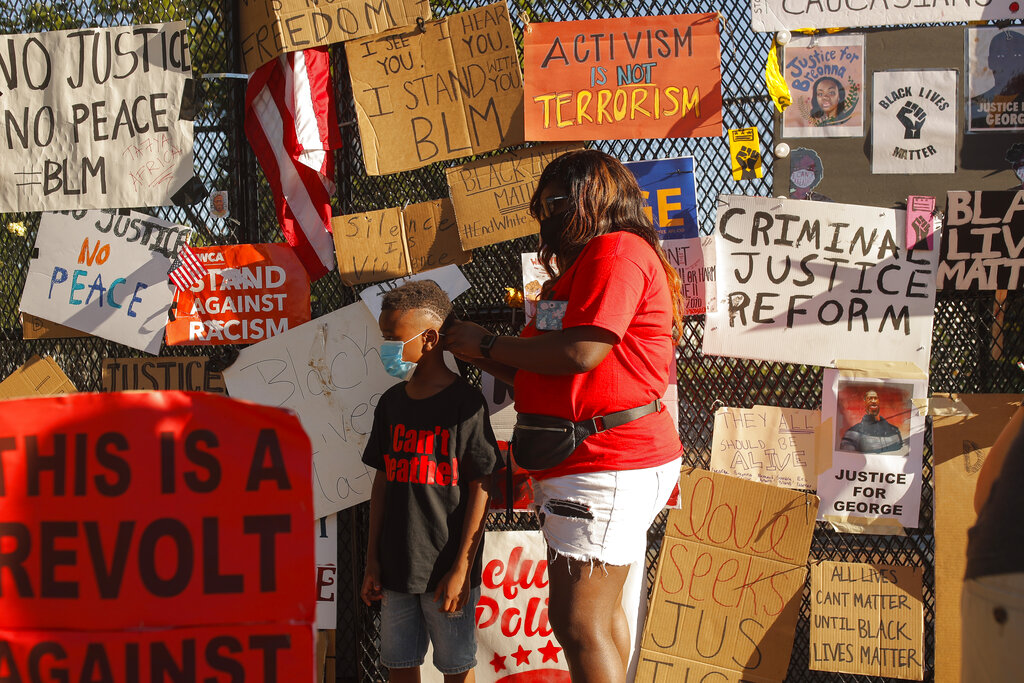 Tiffany West puts a face mask on her nephew as they visit Black Lives Matter Plaza as demonstrations continue Monday, June 8, 2020, near the White House in Washington, over the death of George Floyd, a black man who was in police custody in Minneapolis. Floyd died after being restrained by Minneapolis police officers on May 25. (AP Photo/Maya Alleruzzo)