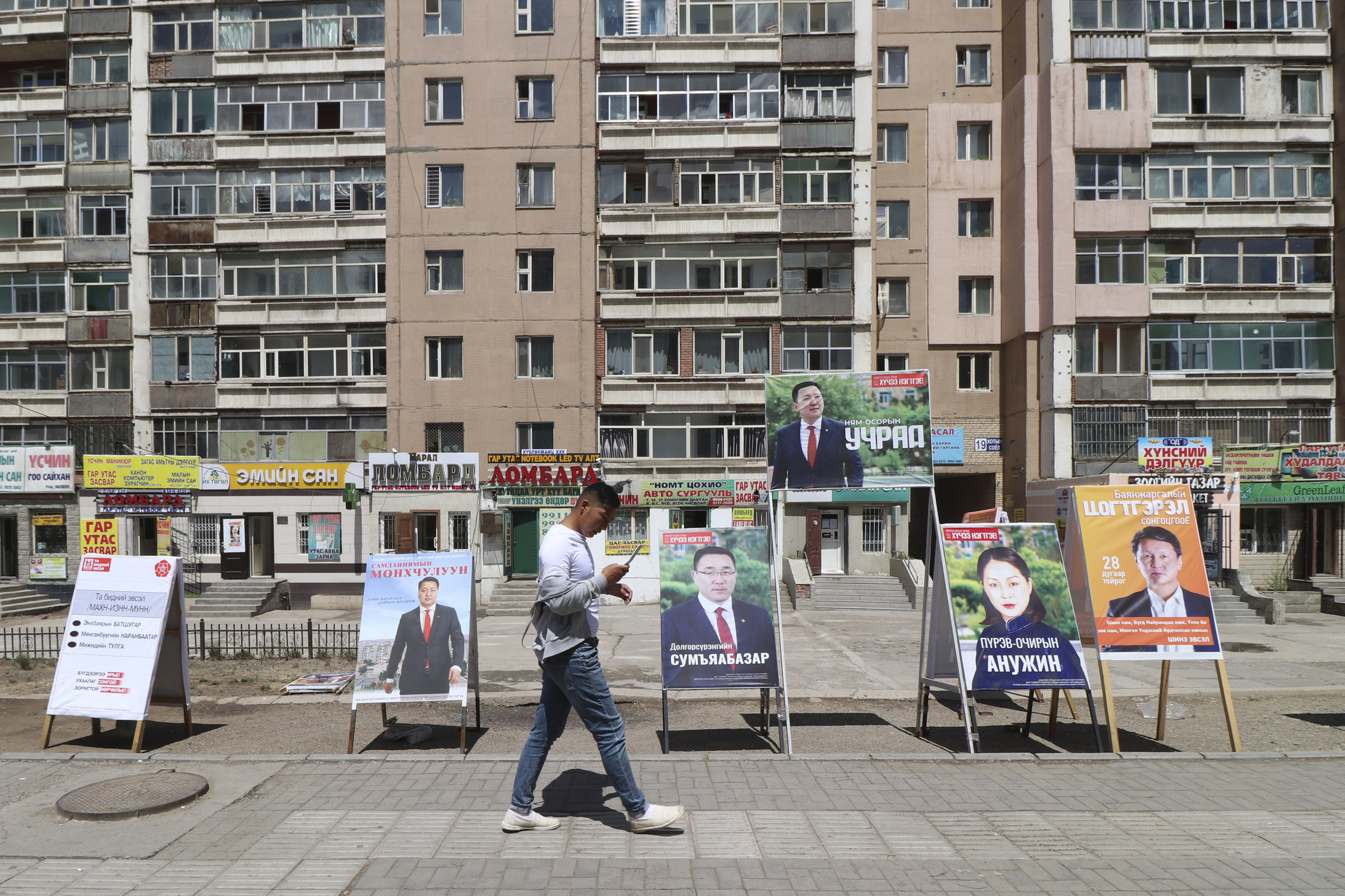 A man walks past election stands of various parties including ruling Mongolian People's Party and independent candidates in the Songinokhairkhan district on the outskirts of Ulaanbaatar, Mongolia, Monday, June 22, 2020. Mongolia holds parliamentary elections on Wednesday, continuing a nearly 30-year democratic system in a vast but lightly populated country sandwiched between authoritarian regimes in Russia and China and beset by economic problems. (AP Photo/Ganbat Namjilsangarav)