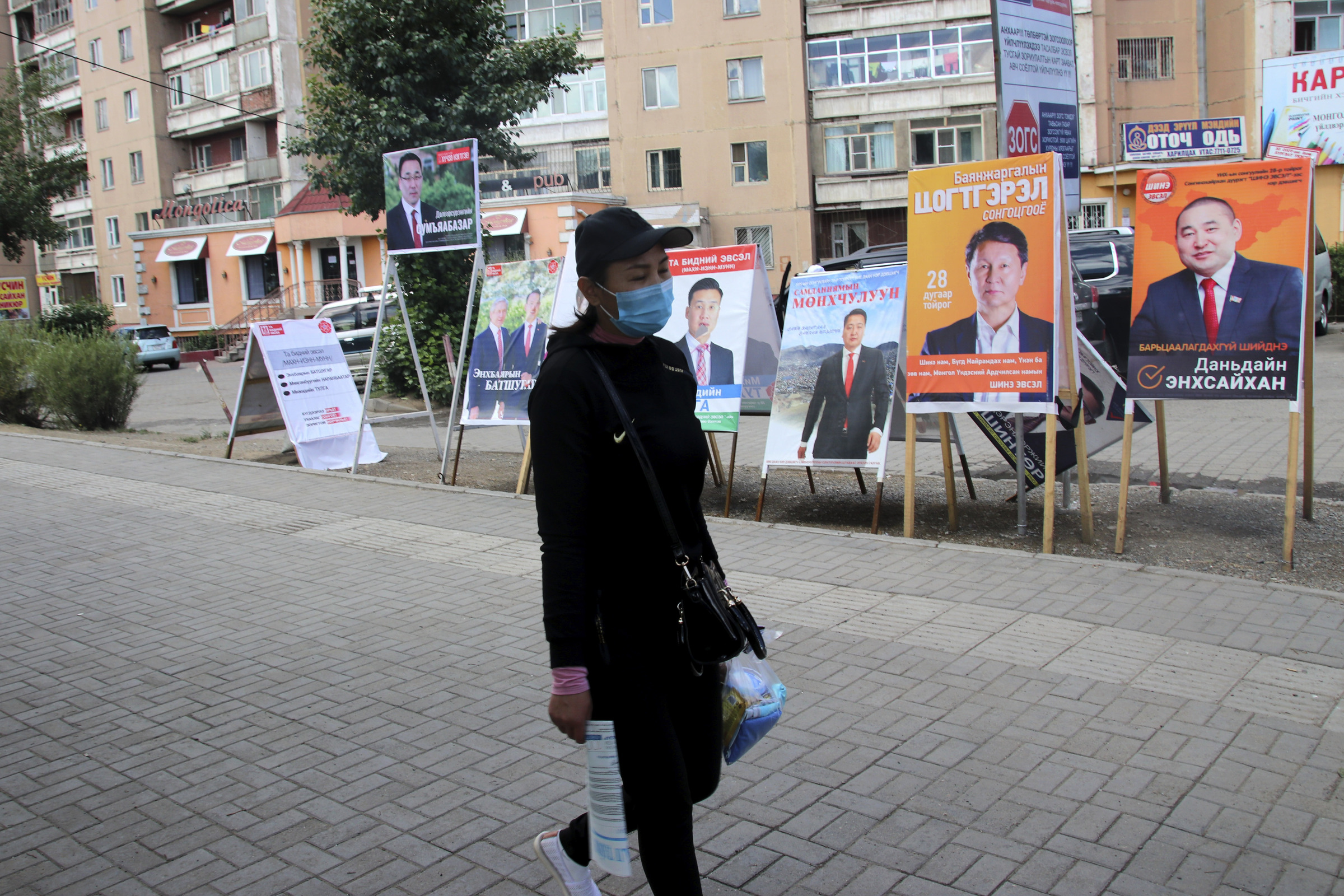 A resident carries groceries past posters and stands of various political party and independent candidates in the Songinokhairkhan district on the outskirts of Ulaanbaatar, Mongolia, Monday, June 22, 2020. Mongolia holds parliamentary elections on Wednesday, continuing a nearly 30-year democratic system in a vast but lightly populated country sandwiched between authoritarian regimes in Russia and China and beset by economic problems. (AP Photo/Ganbat Namjilsangarav)