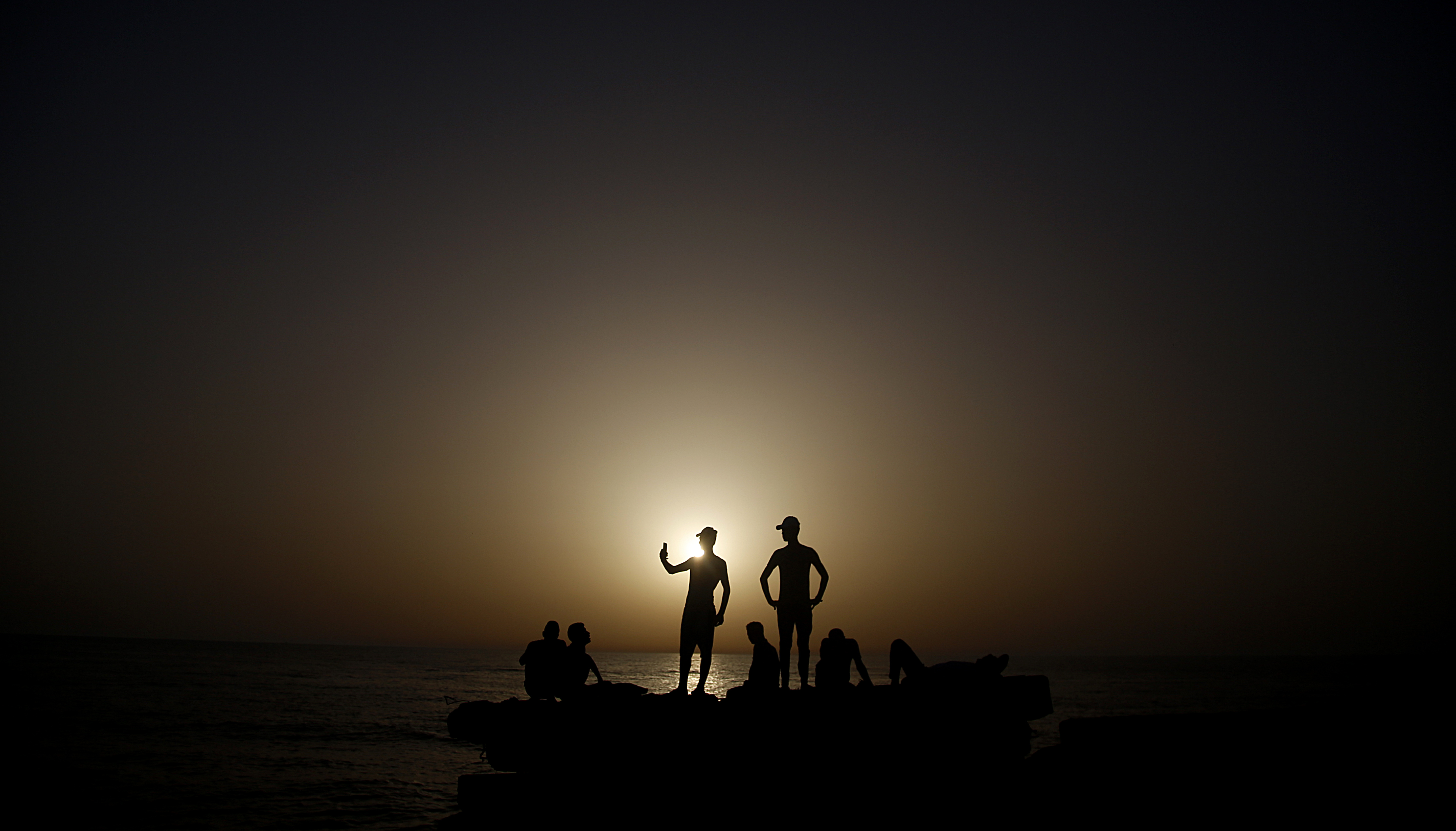 Palestinian men take pictures during sunset at the Gaza port, in Gaza City, Sunday, June 21, 2020. The beach is one of the few open public spaces in this densely populated city. (AP Photo/Hatem Moussa)