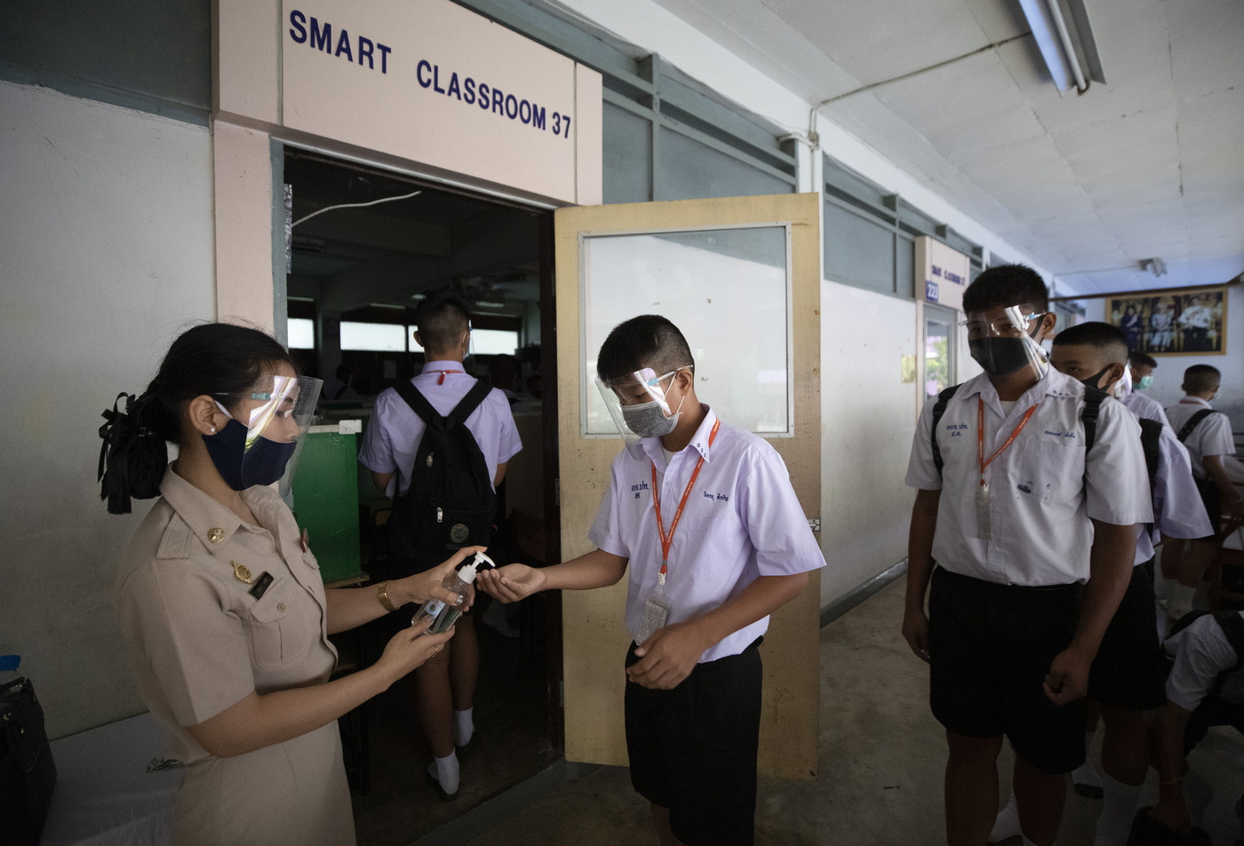 Teacher in protective gear offers hand sanitizer to students before class at the Samkhok School in Pathum Thani, outside Bangkok, Wednesday, July 1, 2020. Thailand has begun a fifth phase of relaxations of COVID-19 restrictions, allowing the reopening of schools and high-risk entertainment venues such as pubs and massage parlors that had been shut since mid-March. (AP Photo/Sakchai Lalit)